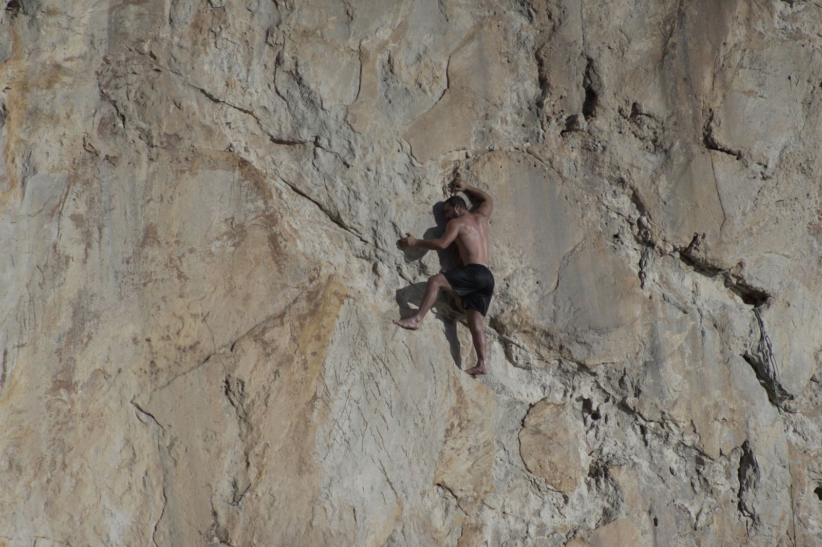 An adventurous man scaling a steep rugged sea cliff under daylight, showcasing extreme sports and determination.