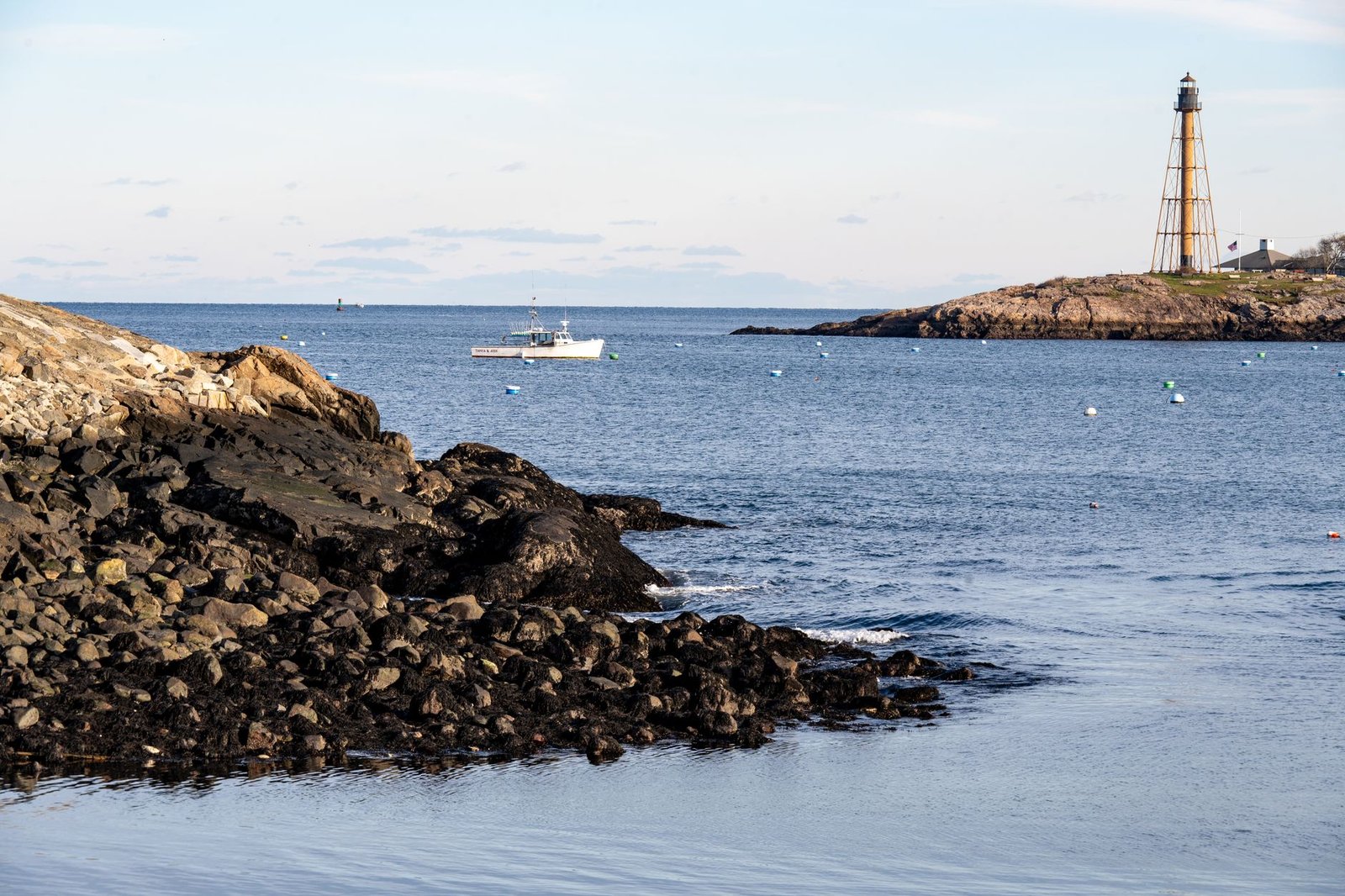 Tranquil coastal scene in Marblehead, Massachusetts, featuring a lighthouse and fishing boat.
