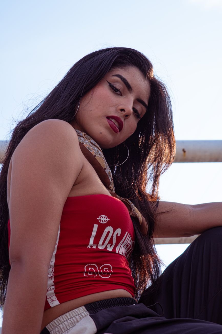 Confident woman poses outdoors in a red 'Los Angeles' top, exuding urban style.