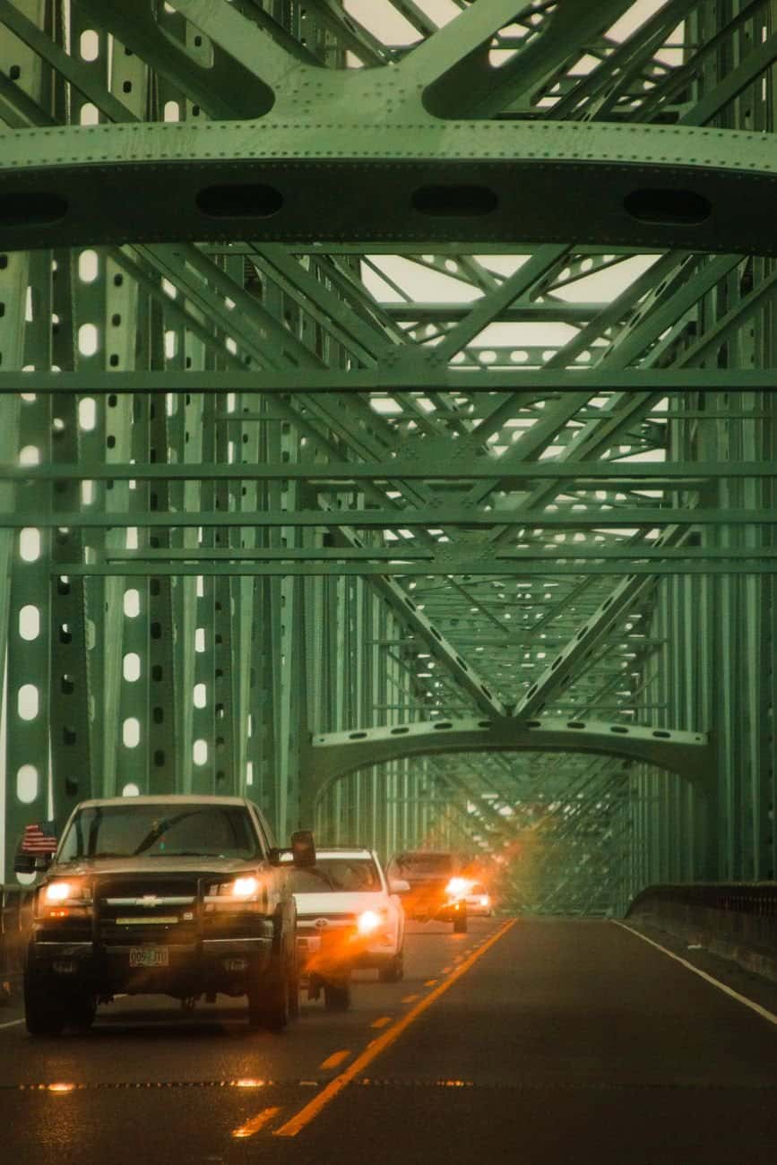 Vehicles drive across a modern green steel suspension bridge, highlighting urban transit and architecture.