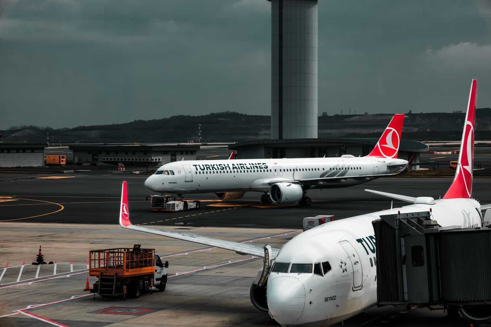 Turkish Airlines planes parked at an airport with a control tower in the background.