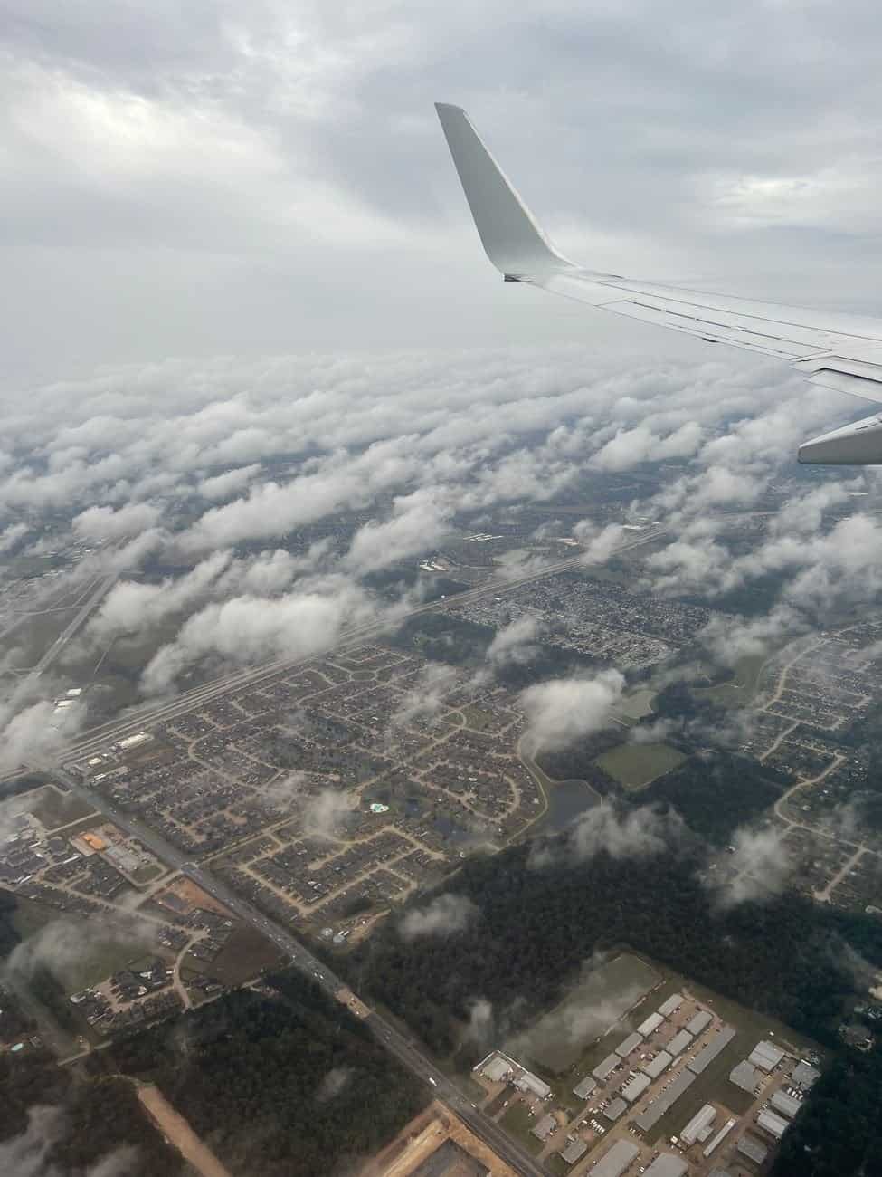 Aerial view of suburban area surrounded by clouds, captured from an airplane.