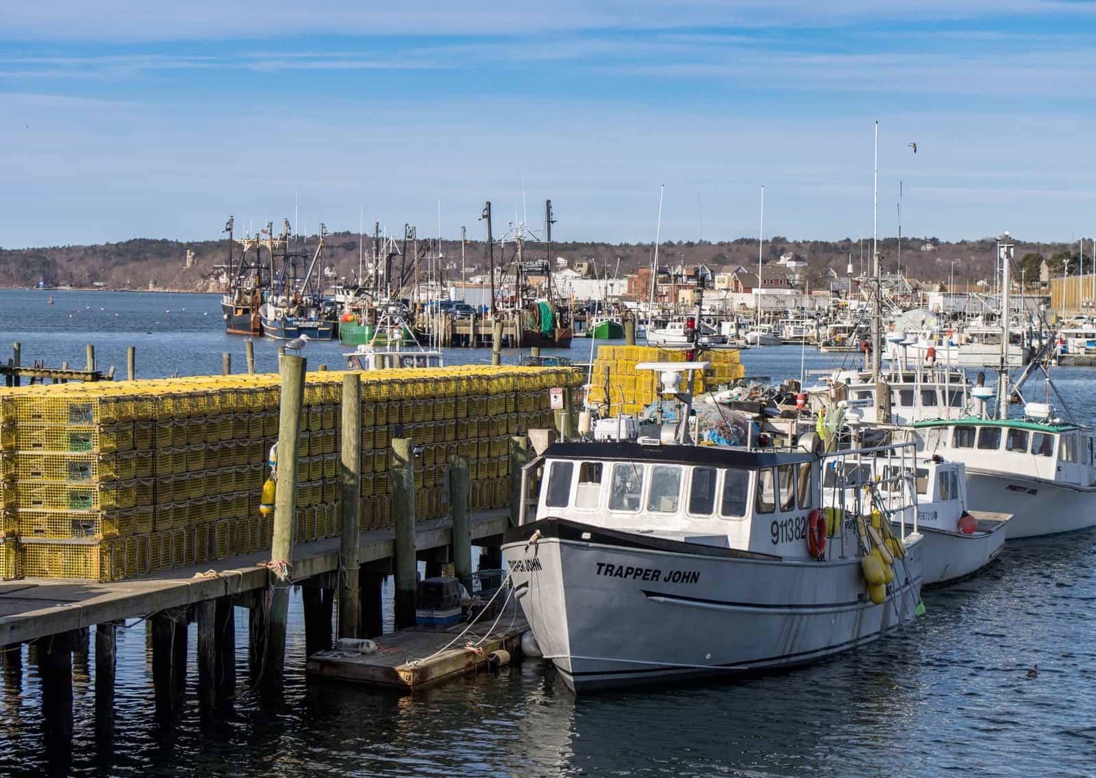 Coastal harbor view with moored fishing boats and lobster traps in bright sunlight.