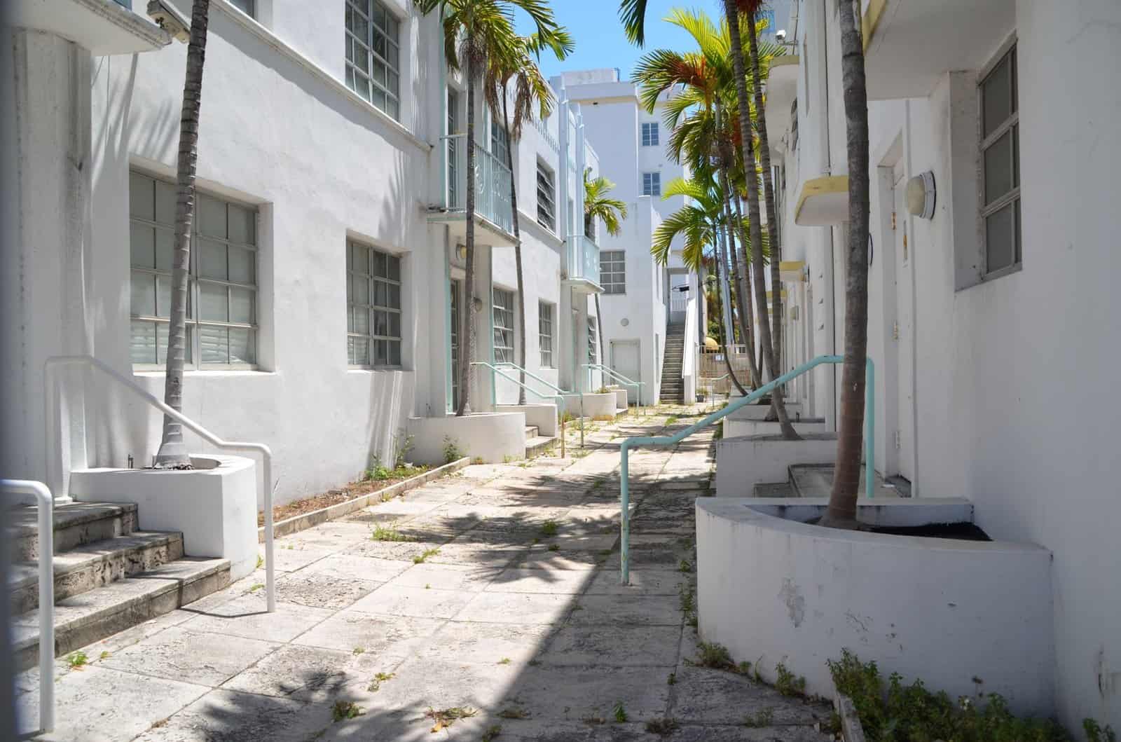 Empty alley with art deco architecture in Miami, Florida, featuring palm trees and sunlight.