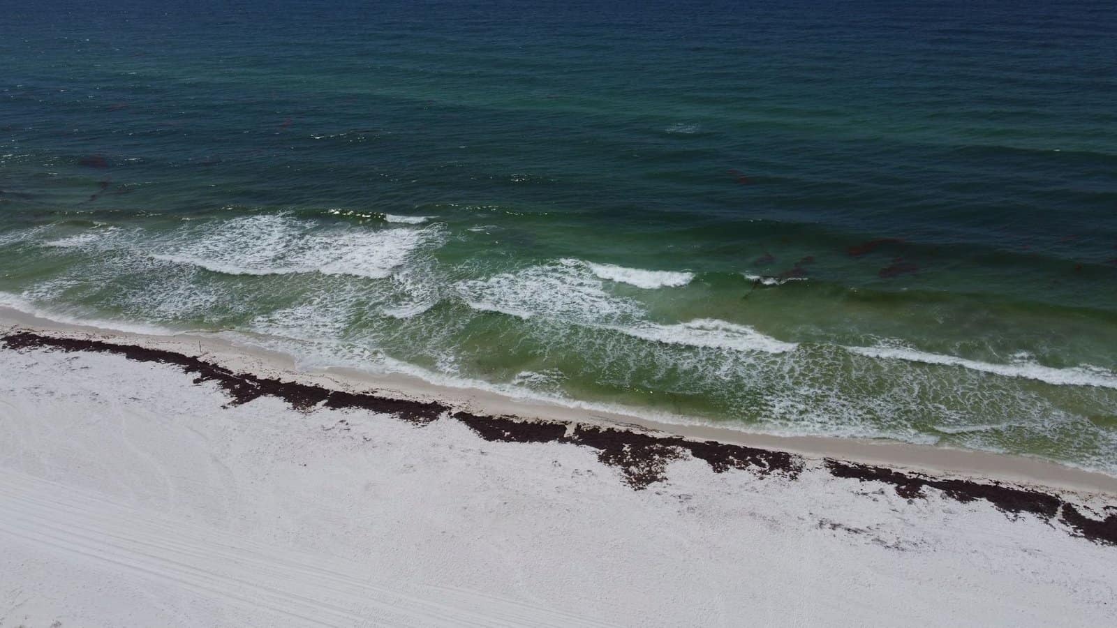 Aerial view of the pristine Pensacola Beach with waves crashing onto the shore under a summer sky.