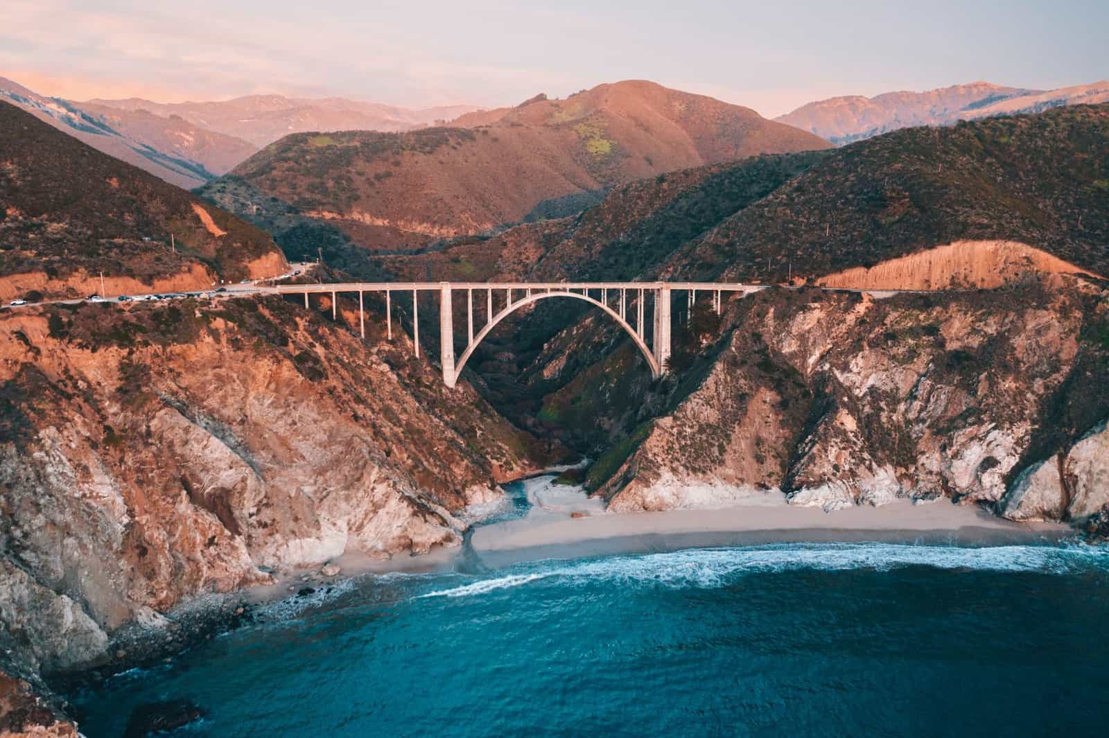 Stunning aerial shot of Bixby Creek Bridge in California during sunset, capturing the rugged coastline and blue ocean.