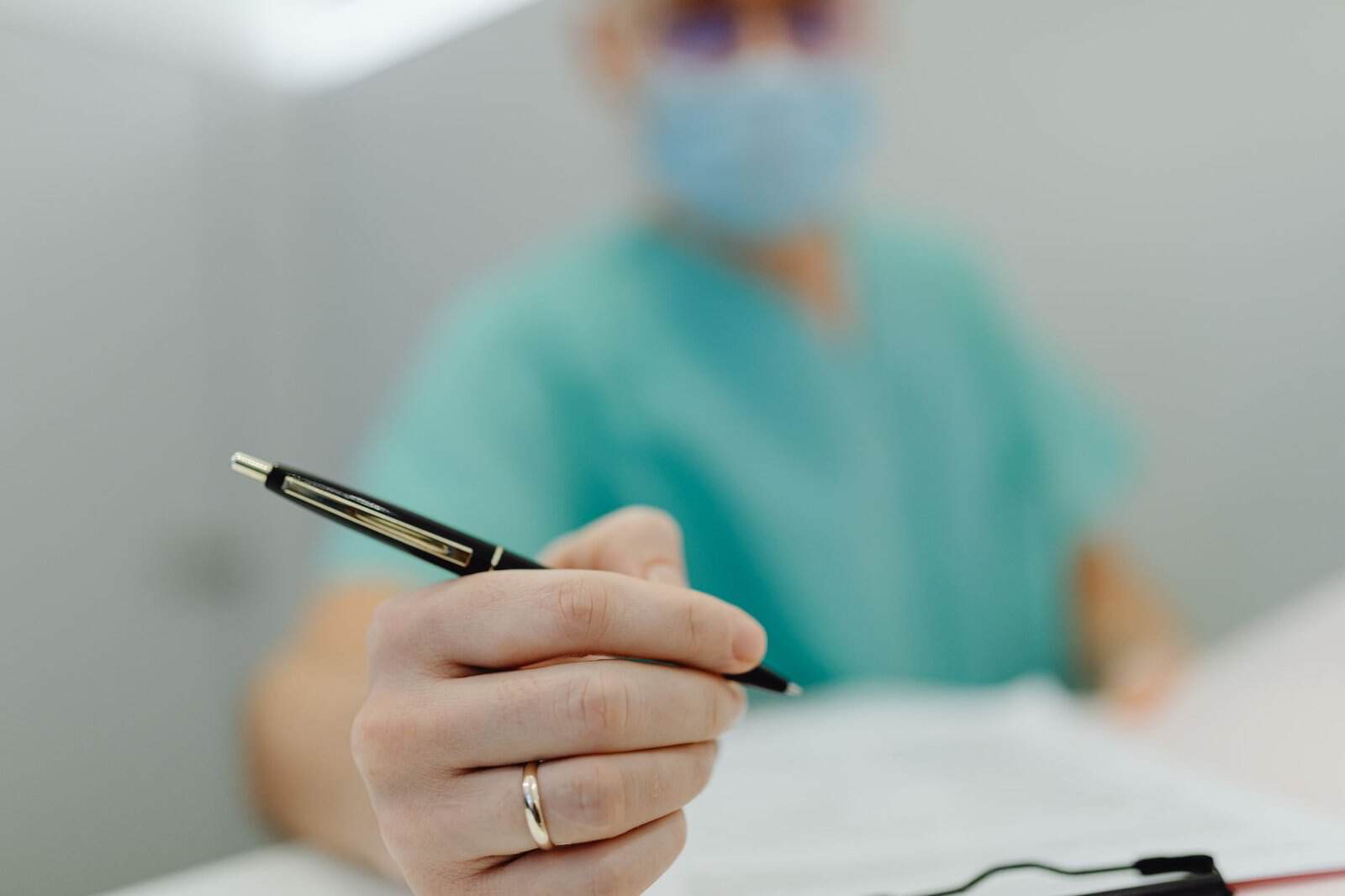 Close-up of a medical professional in scrubs writing with a pen, showing focus on hand and pen.