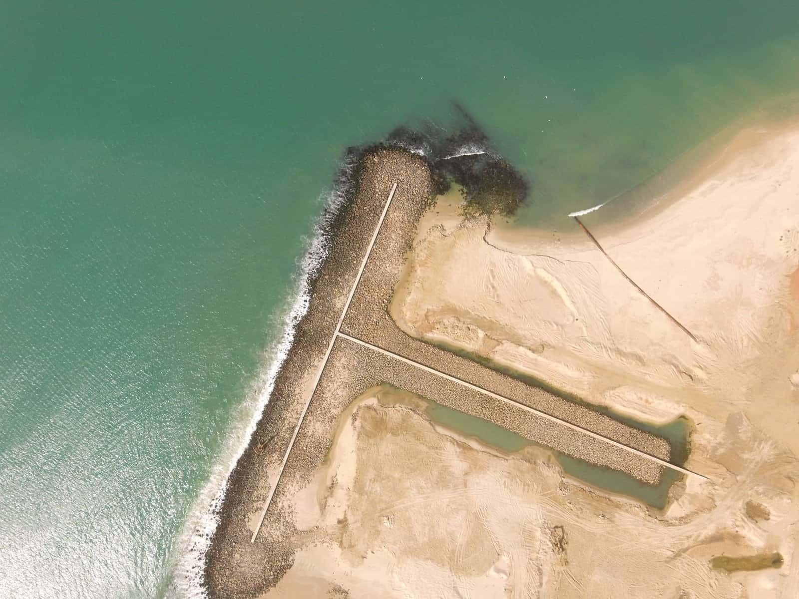 Drone aerial view of a sandy coastline and jetty in Mauritania during the day.