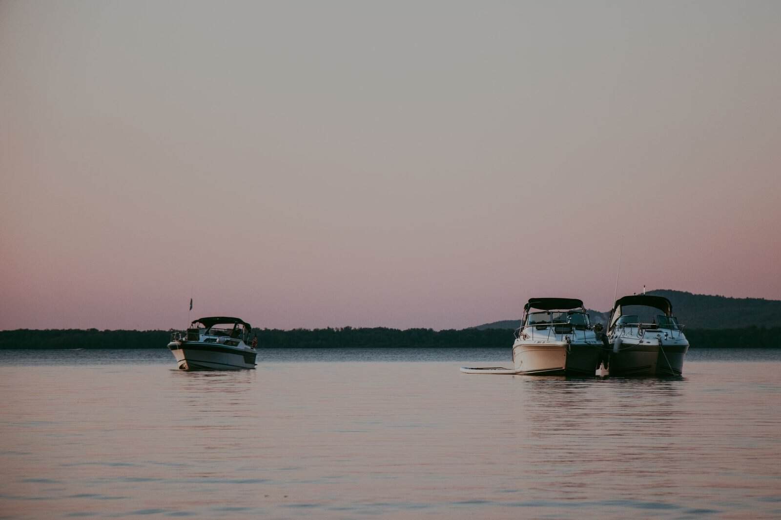 Three boats anchored on a tranquil lake during a beautiful sunset.
