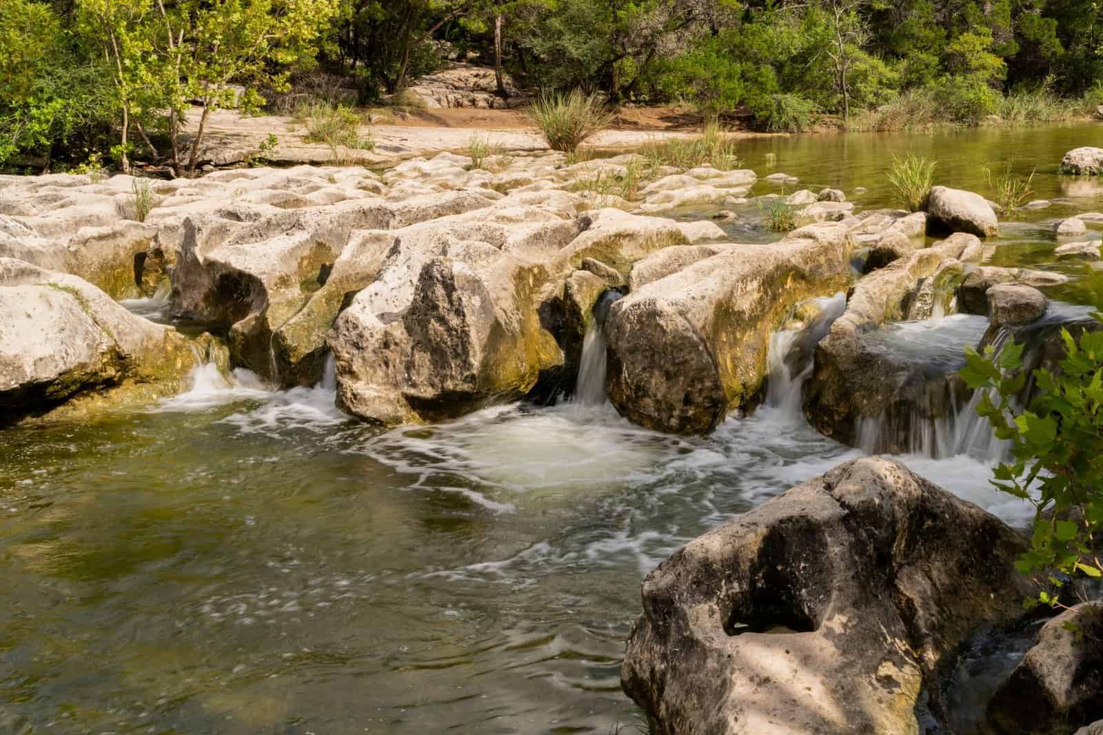 A tranquil stream flowing over natural rock formations surrounded by lush greenery.