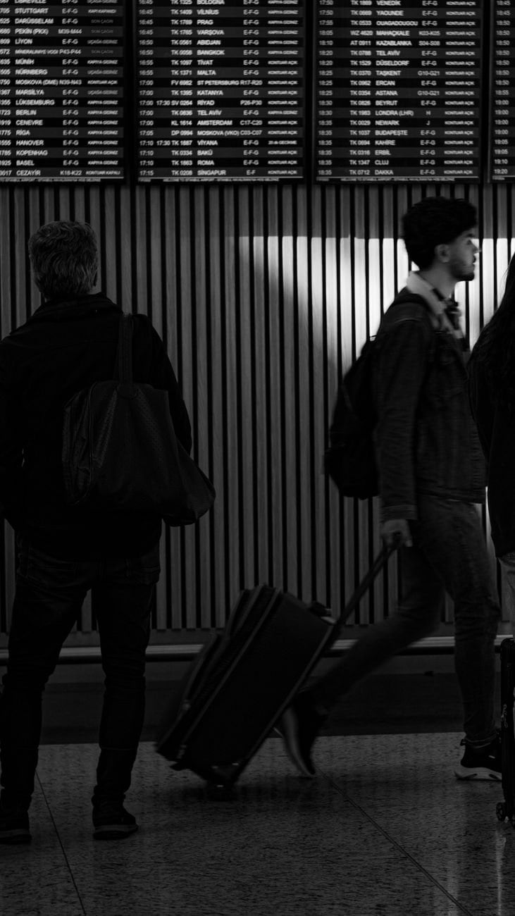 Black and white image showing travelers with luggage in İstanbul airport terminal.