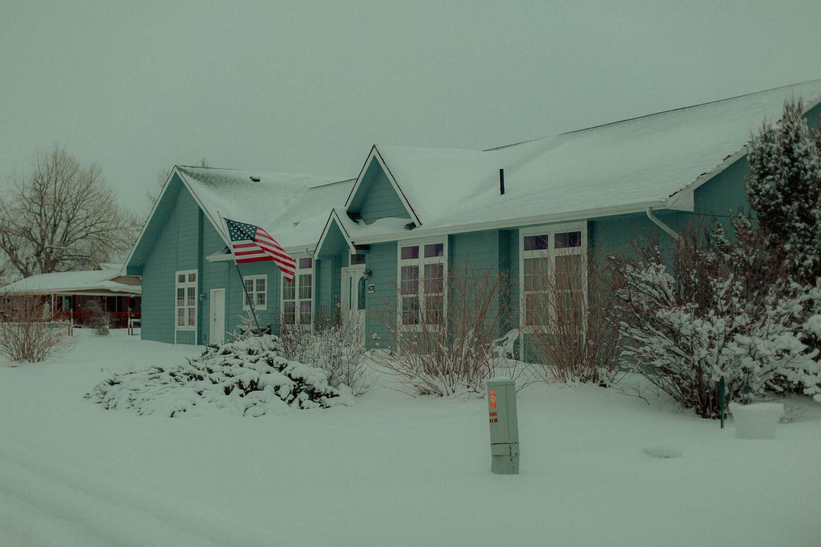 Snow-covered house with American flag in a serene winter landscape.