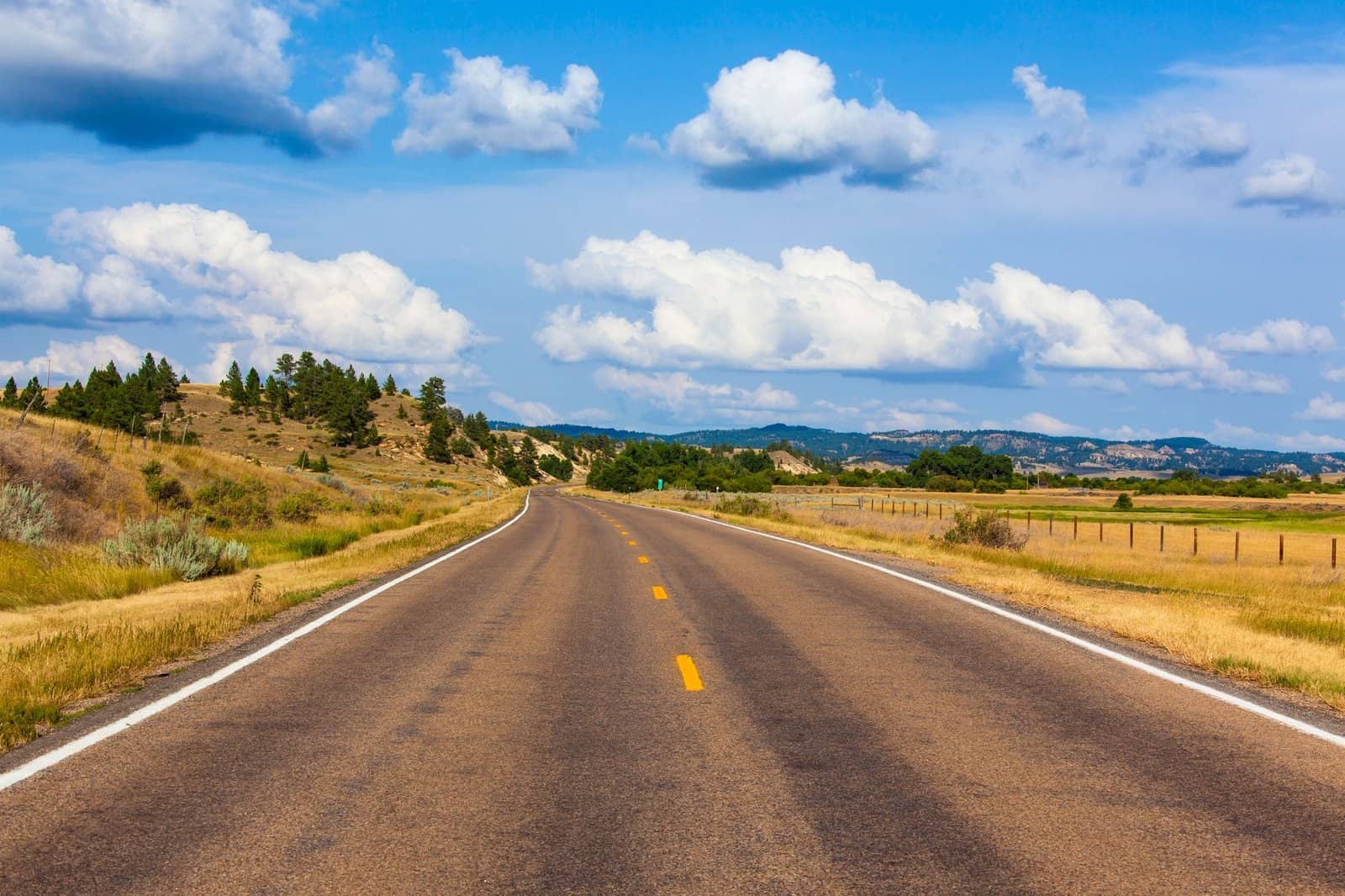A picturesque highway stretches through Montana, surrounded by rolling landscapes and a clear blue sky.