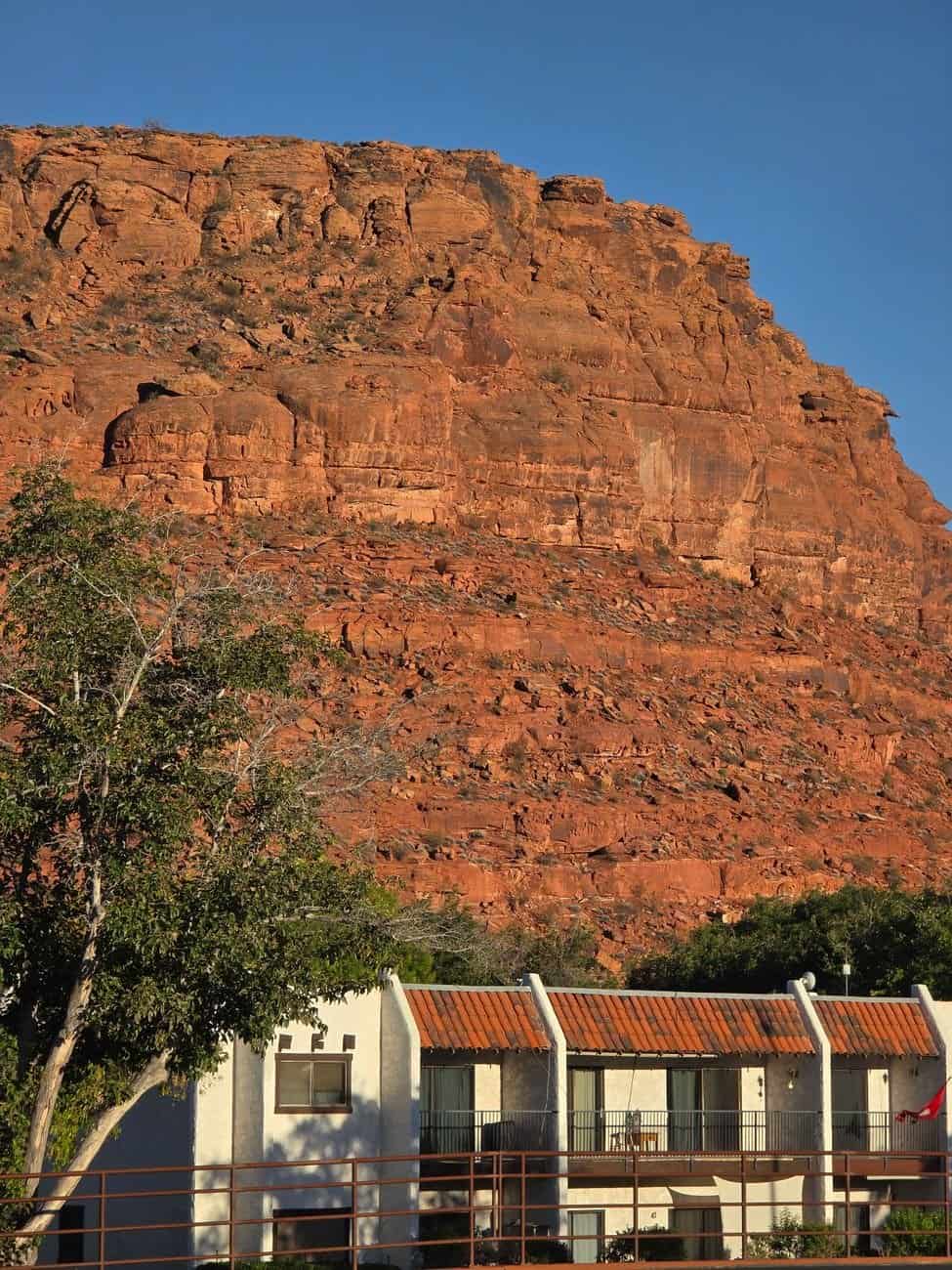 Charming houses nestled against striking red rock cliffs under a clear sky.