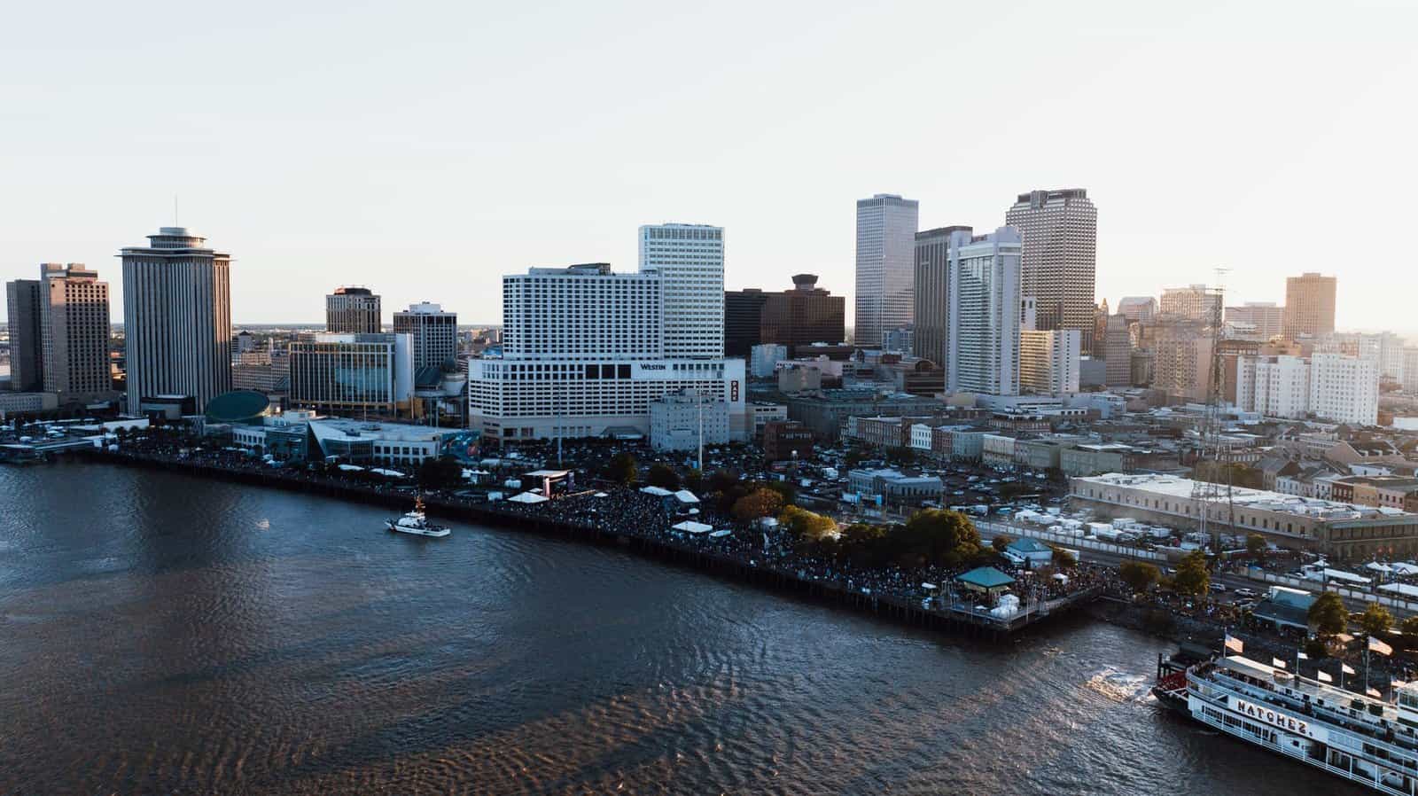 Drone shot capturing the bustling cityscape of New Orleans and the Mississippi River at dusk.