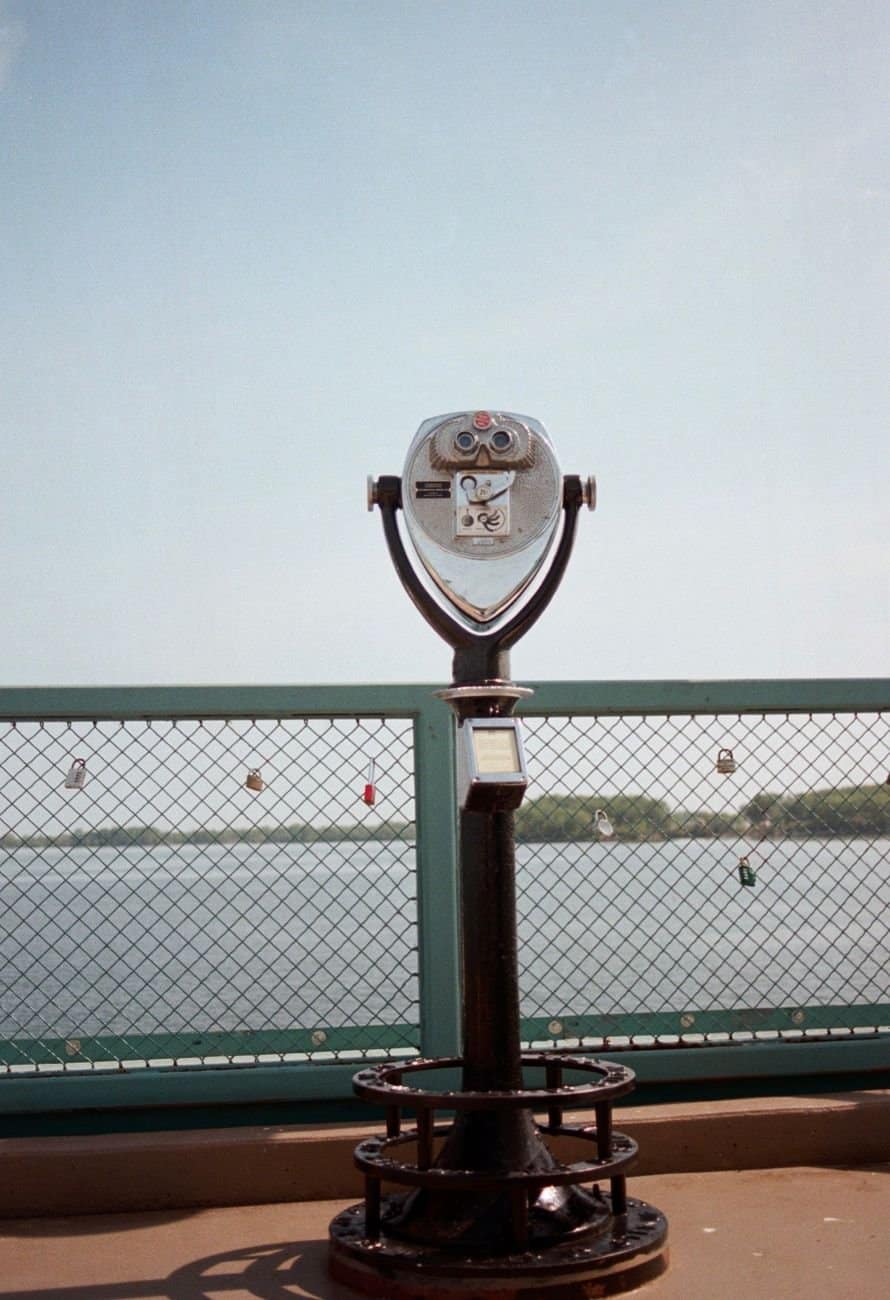 Coin-operated viewer on a pier railing in Erie, PA, overlooking Lake Erie with padlocks in view.