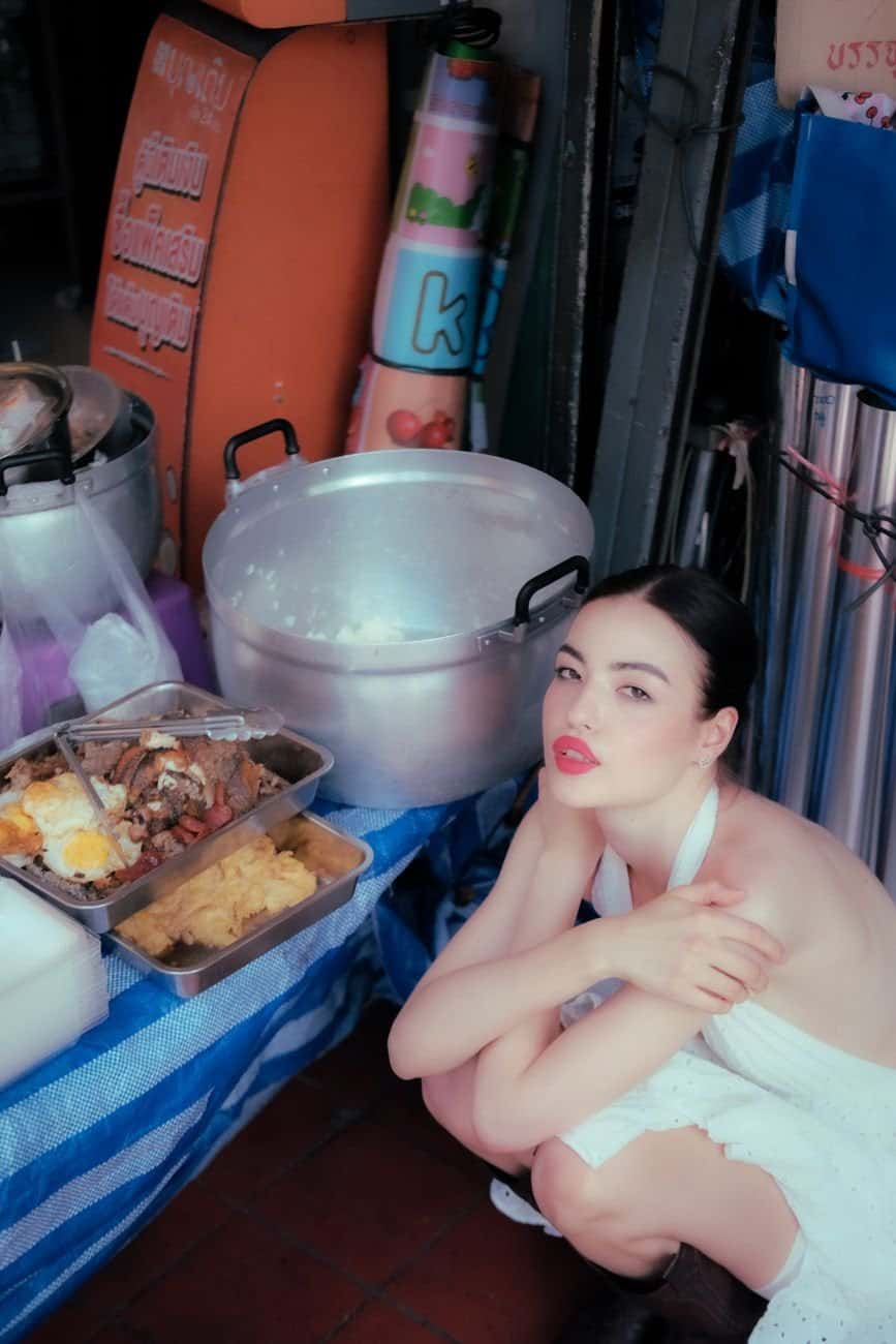 A woman sitting beside street food stalls in a vibrant Bangkok market.