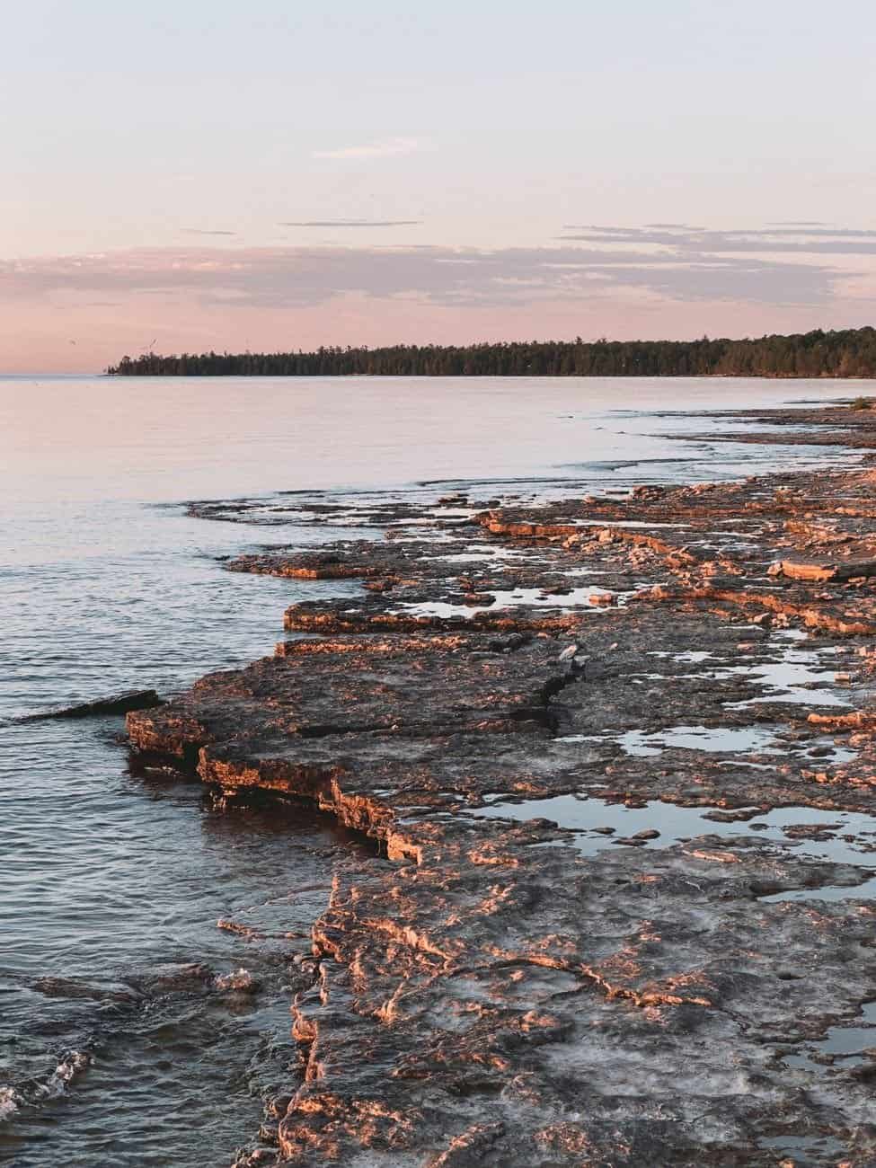 Peaceful sunset over rocky shoreline in Wisconsin, USA, reflecting serene evening hues.