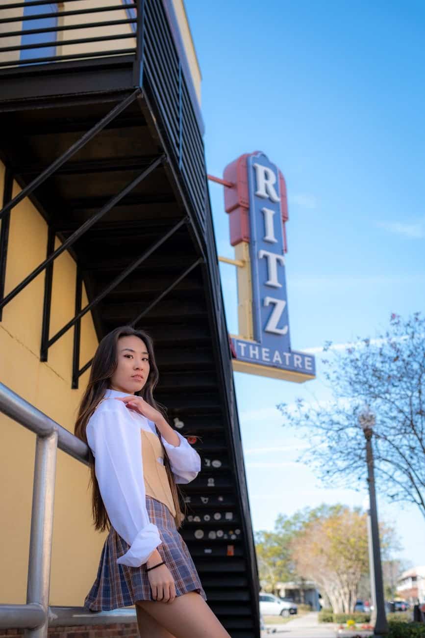 Asian woman posing fashionably in front of Ritz Theatre sign in city environment.