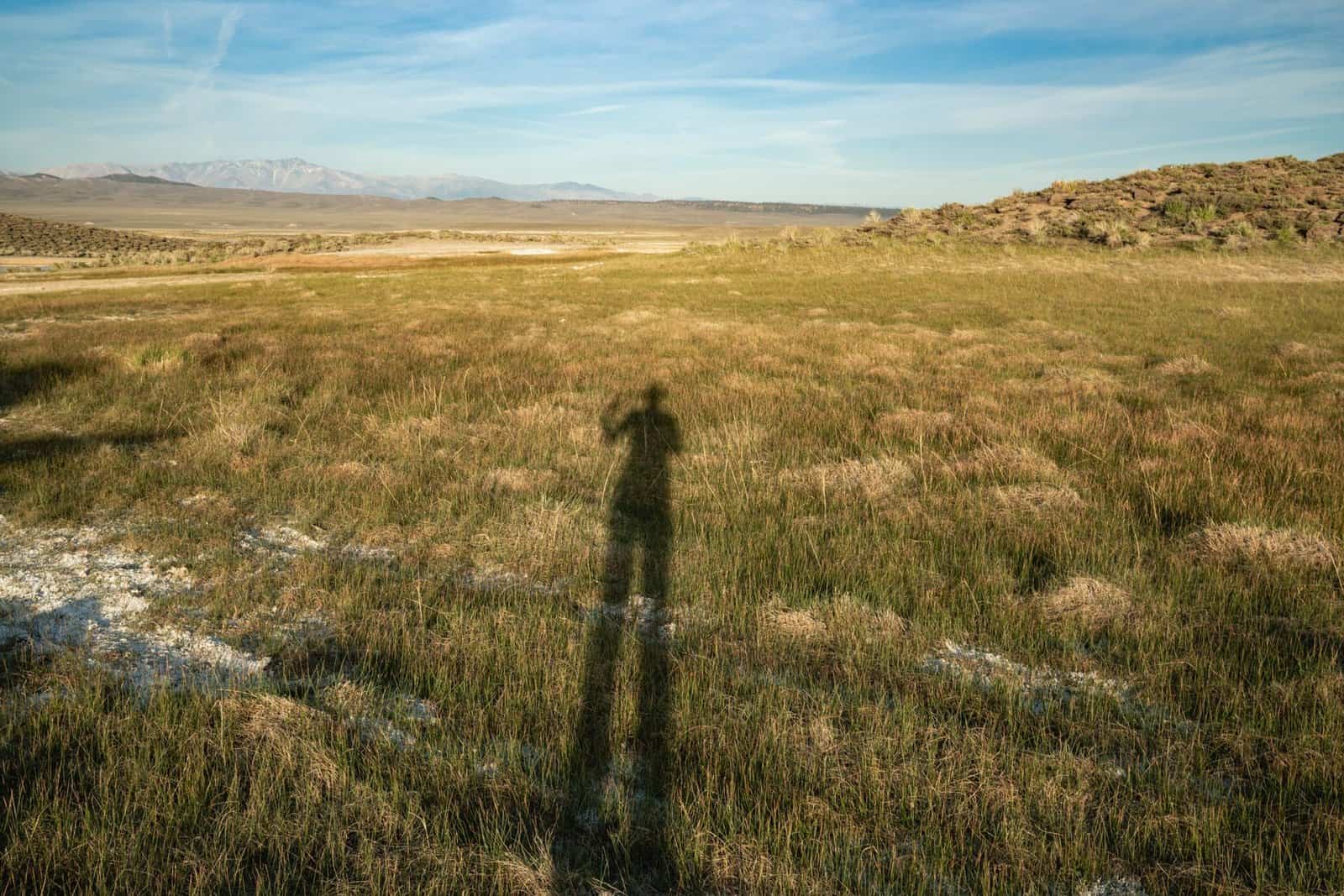 A large grassy field with distant mountains and a shadow cast by the sun setting in the clear sky.