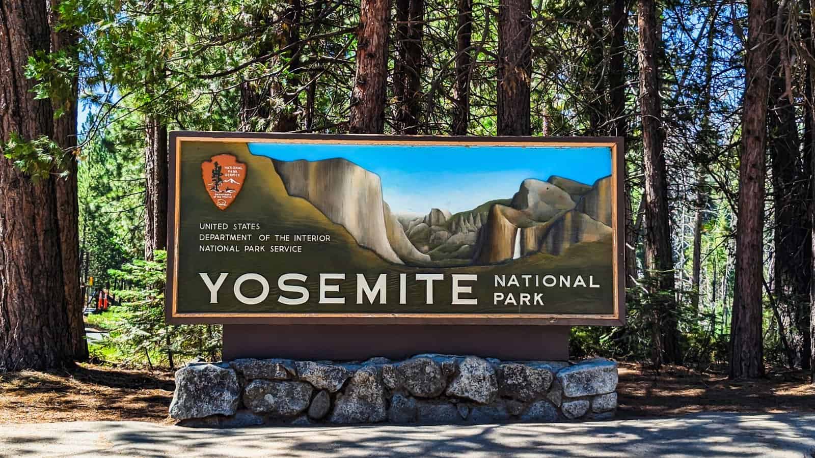 Yosemite National Park entrance sign set against a backdrop of towering trees.
