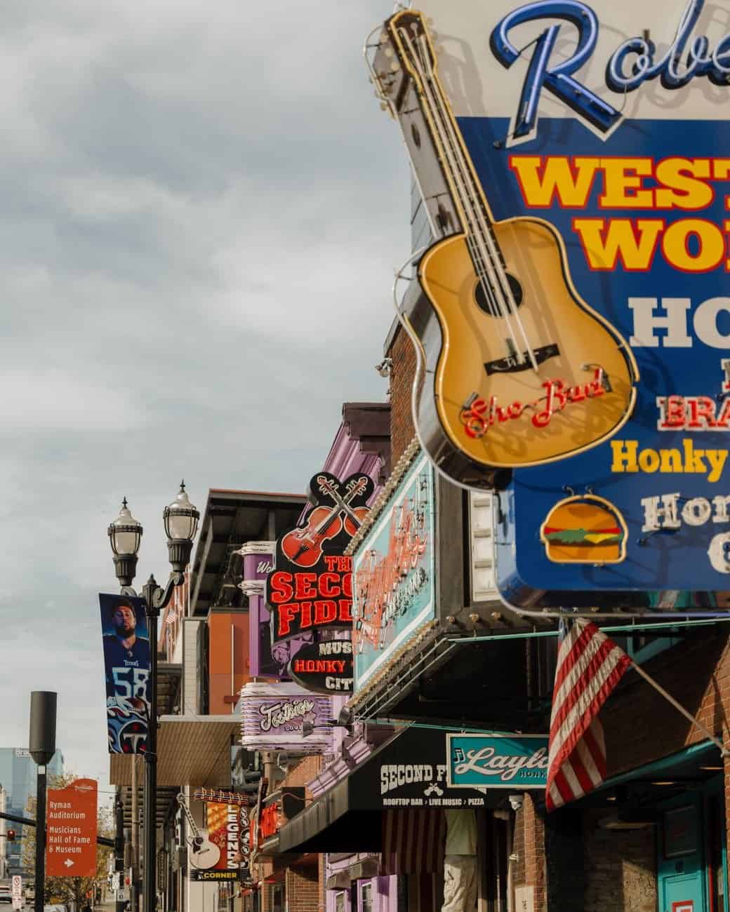 Vibrant Nashville street with colorful neon signs under a cloudy sky.