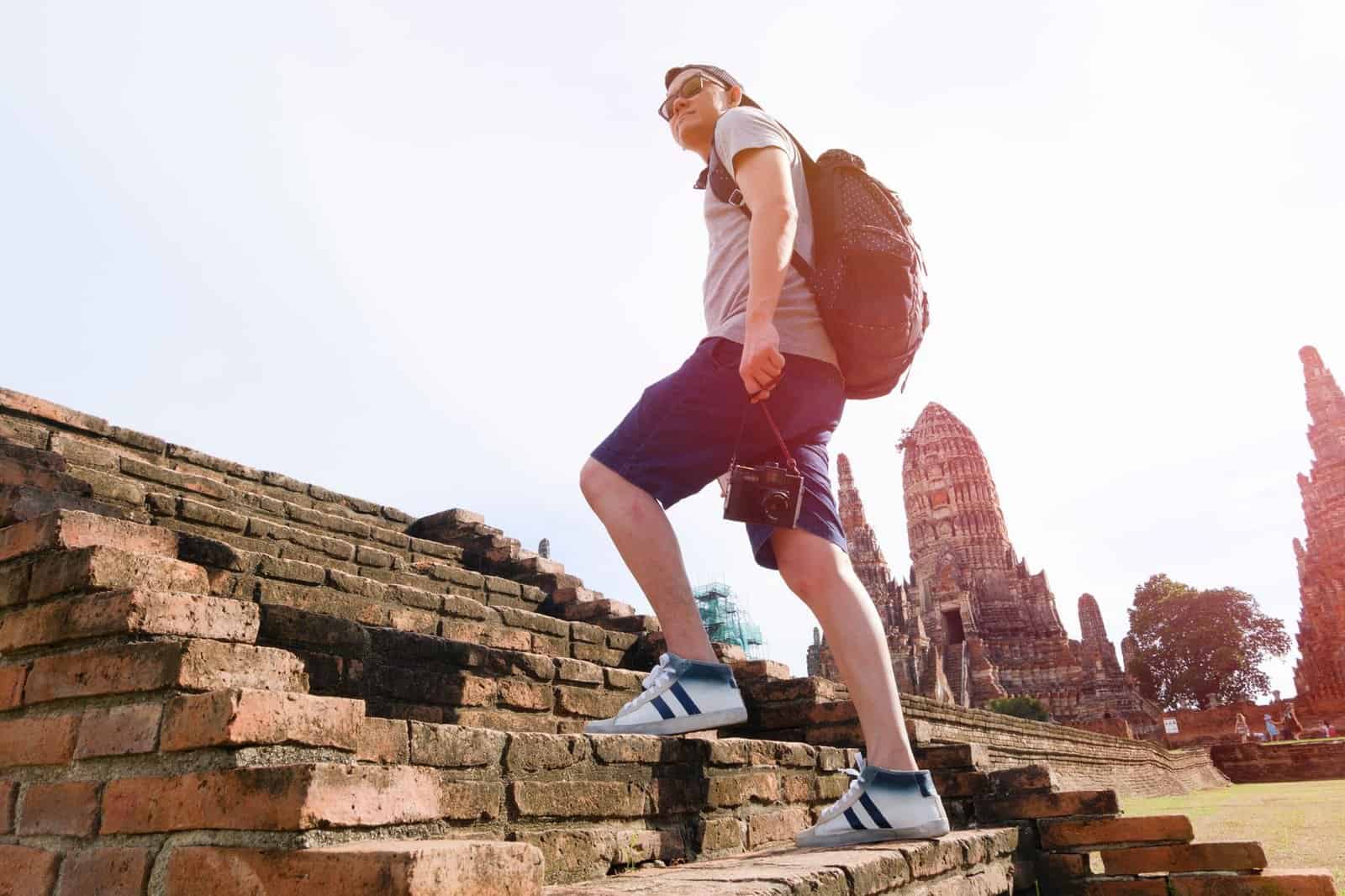 A tourist climbs brick steps at a historic temple site under a bright sky, capturing adventure and exploration.