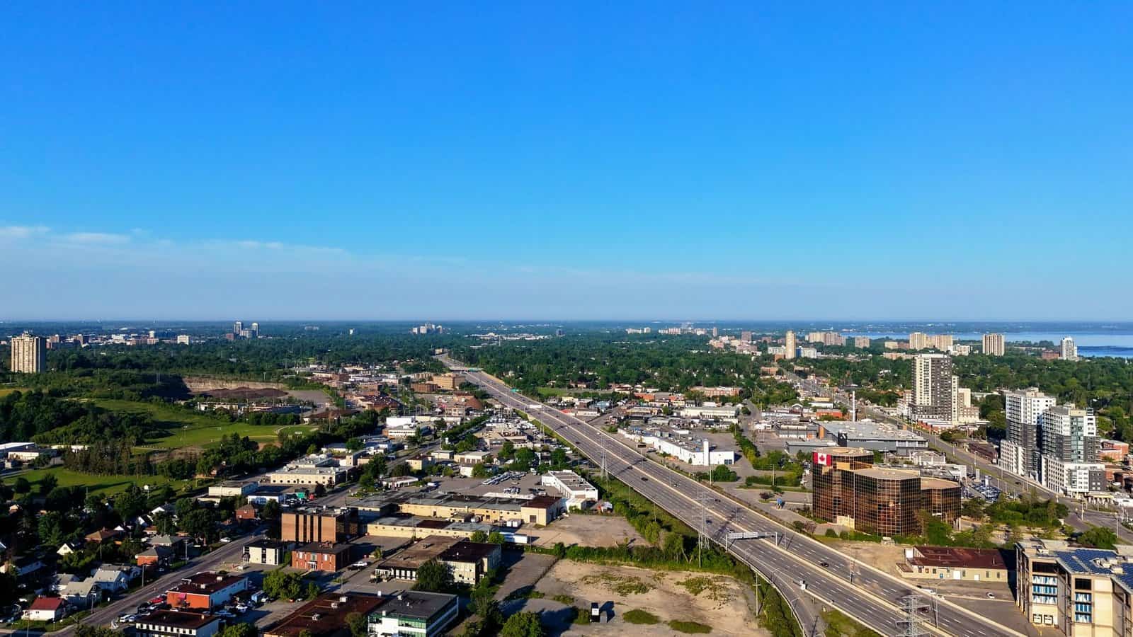 Aerial view of a cityscape with highway, buildings, and greenery under a clear blue sky.