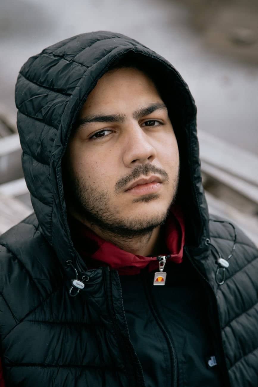 High angle of young bearded male in warm clothes looking at camera while standing on street