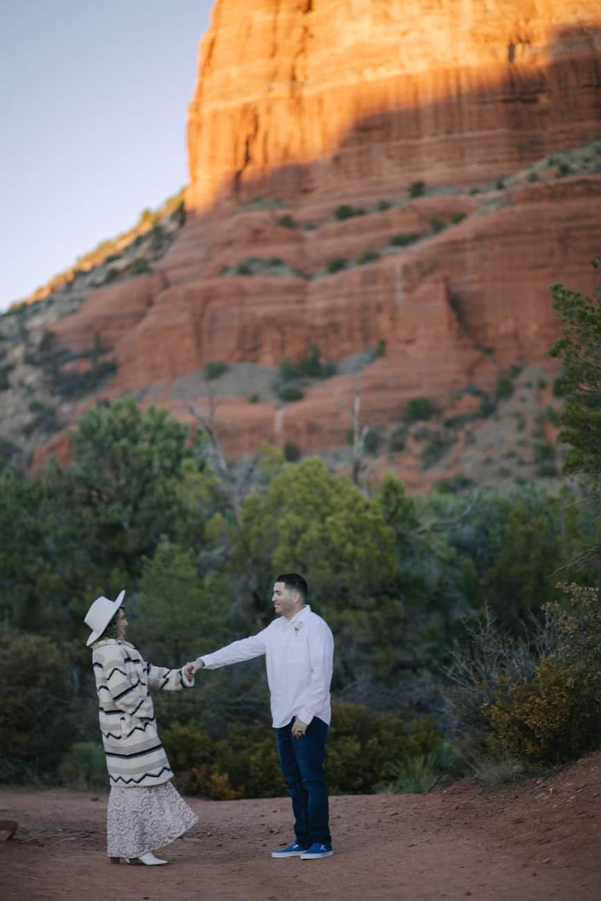 A couple holding hands in front of Sedona's iconic red rock formations, embracing nature.
