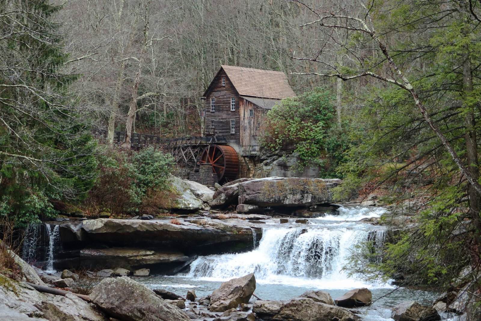 A picturesque grist mill beside a flowing waterfall in a lush forest setting.