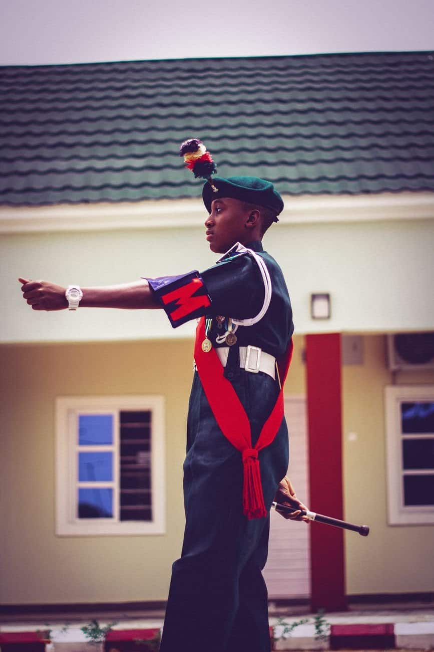 A young cadet stands proudly in traditional uniform in front of a building.