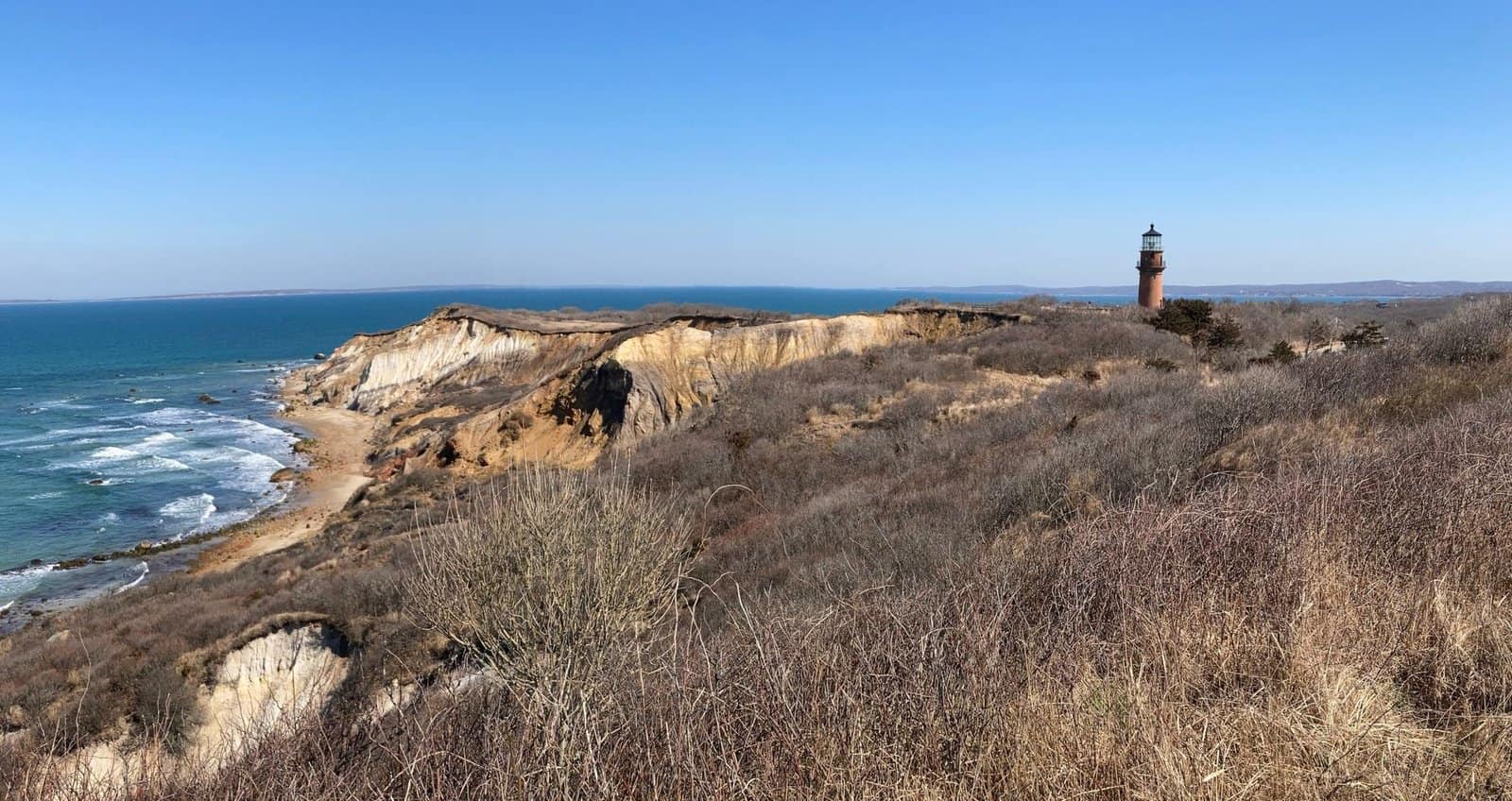 Beautiful coastal scenery with the Aquinnah lighthouse and cliffs under a clear blue sky.