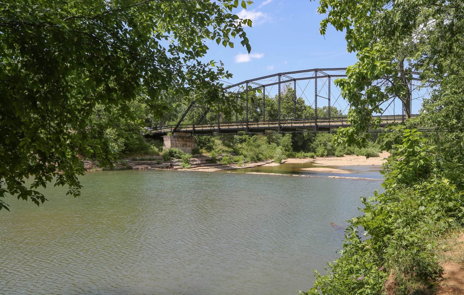 A picturesque view of War Eagle Bridge spanning a serene river surrounded by lush greenery in Arkansas.