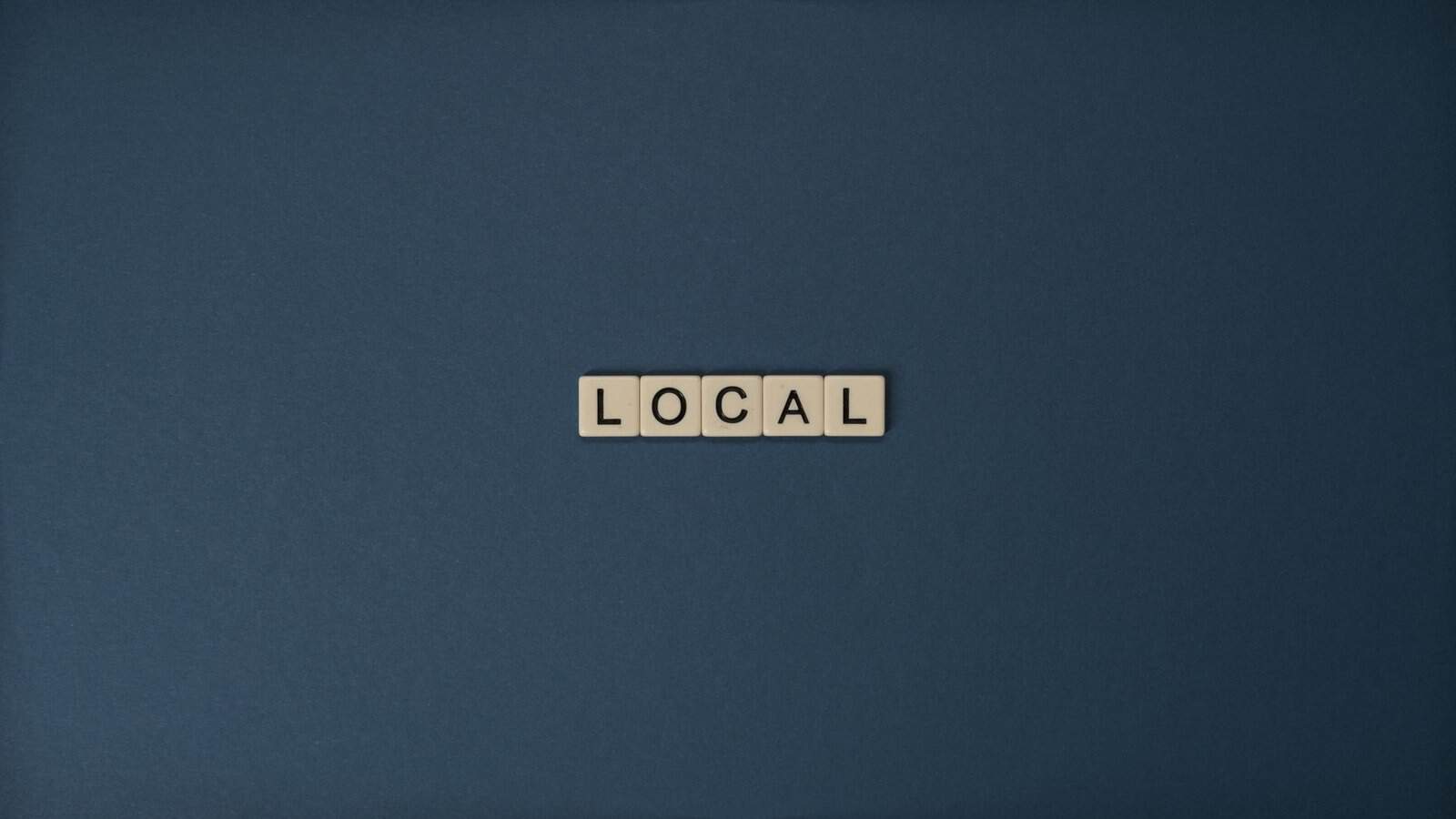 Flat lay of 'Local' in Scrabble tiles on a blue background, with ample copy space.