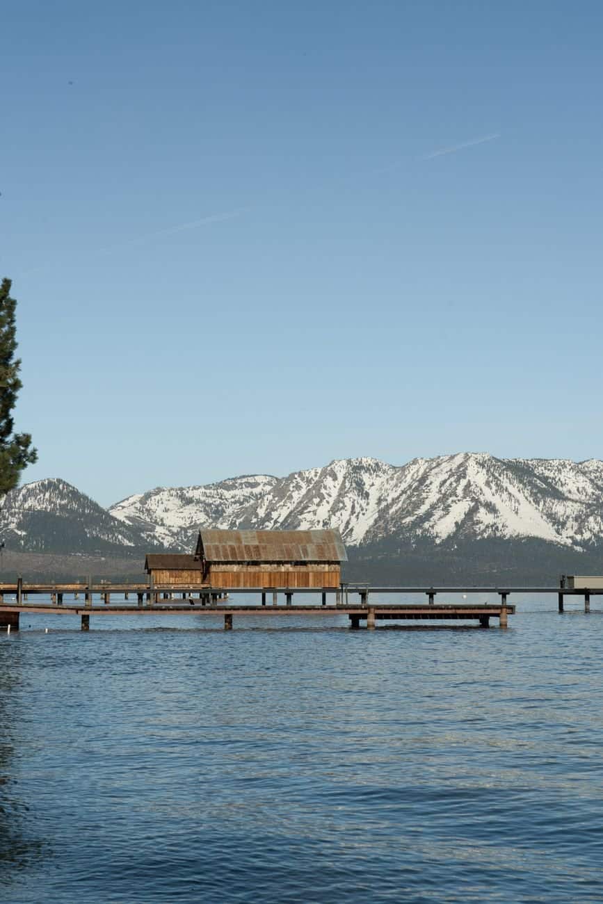 A tranquil view of Lake Tahoe with a wooden pier and snow-covered mountains under a clear sky.