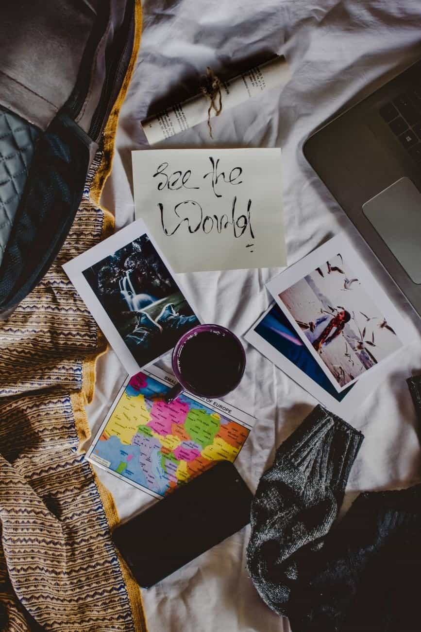 Flat lay of travel planning essentials on a bed, including photos, map, and a laptop.