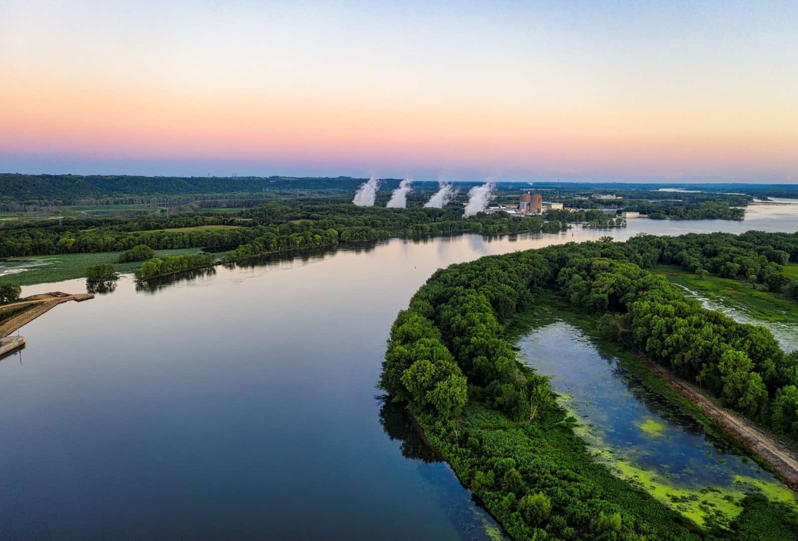 Aerial shot of the Mississippi River with lush greenery and distant smoke at dusk, near Welch, MN.