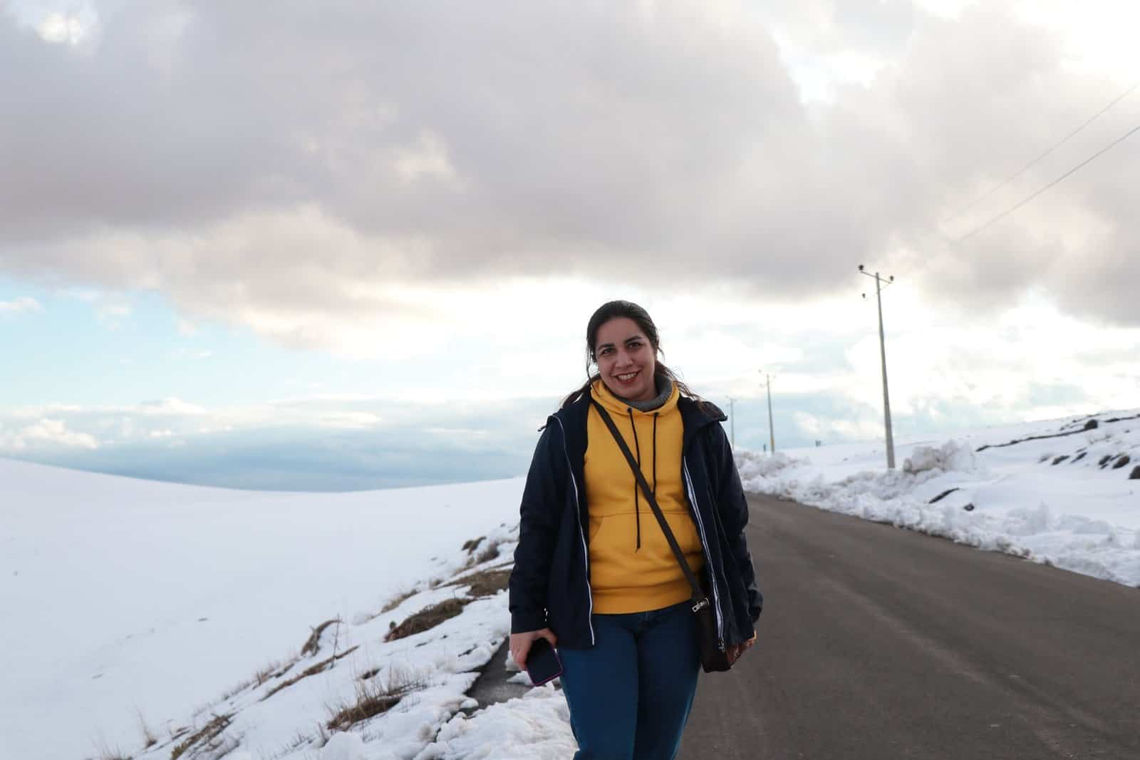 A cheerful young woman enjoying a winter day on a snow-covered road under a dramatic cloudy sky.