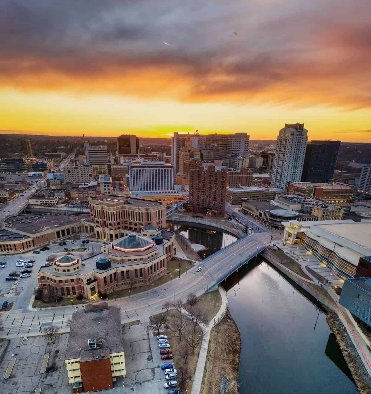 Aerial view of Rochester, Minnesota's skyline at sunset with vibrant city lights reflecting on the water.