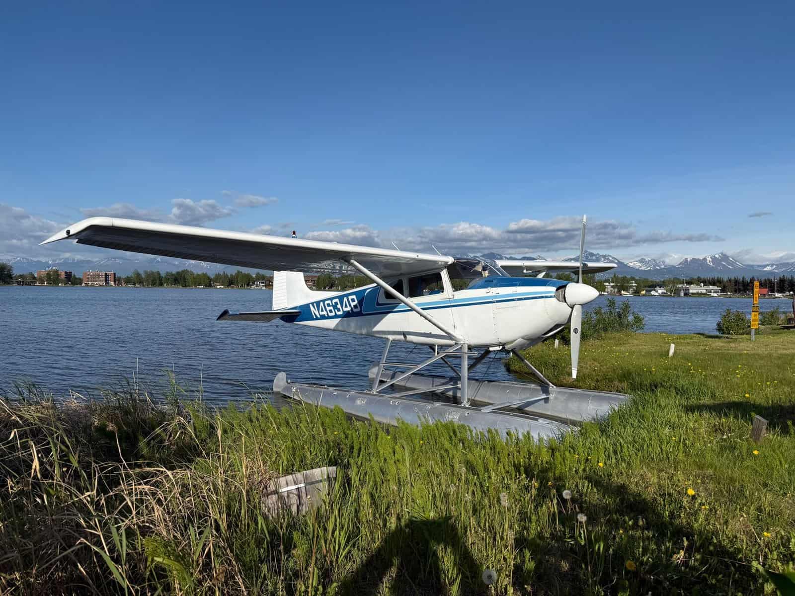 A scenic view of a seaplane docked by a lake, framed by distant mountains under a blue sky.