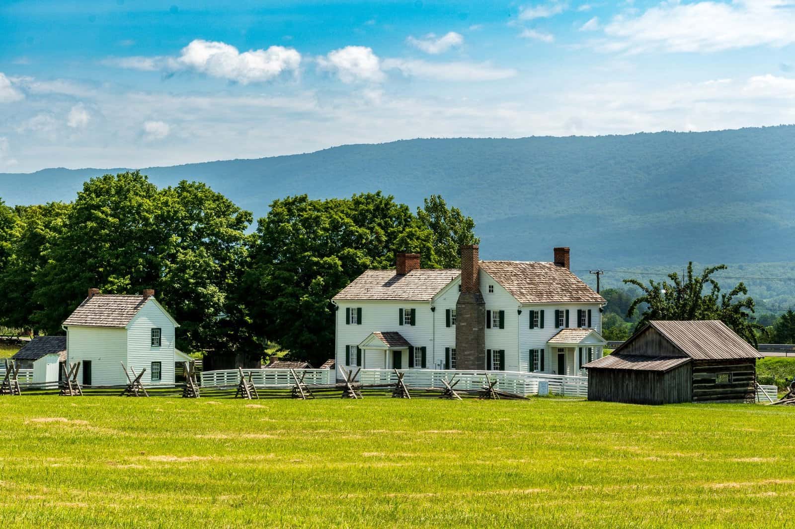 Idyllic rural farmhouse set against a vibrant summer landscape with lush greenery and mountain views.