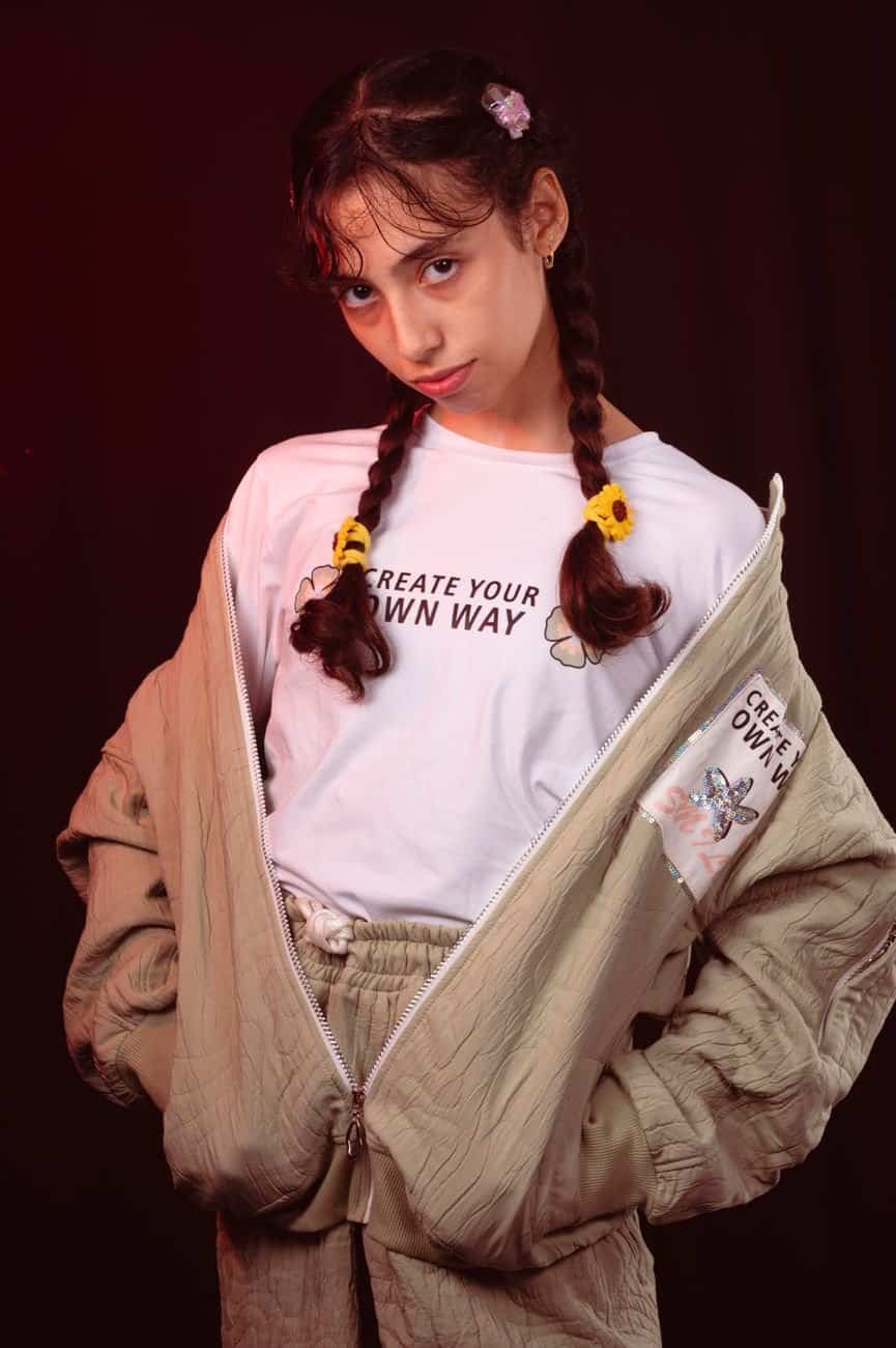 Young girl with braided hair wearing a fashionable outfit and statement shirt, exuding confidence.