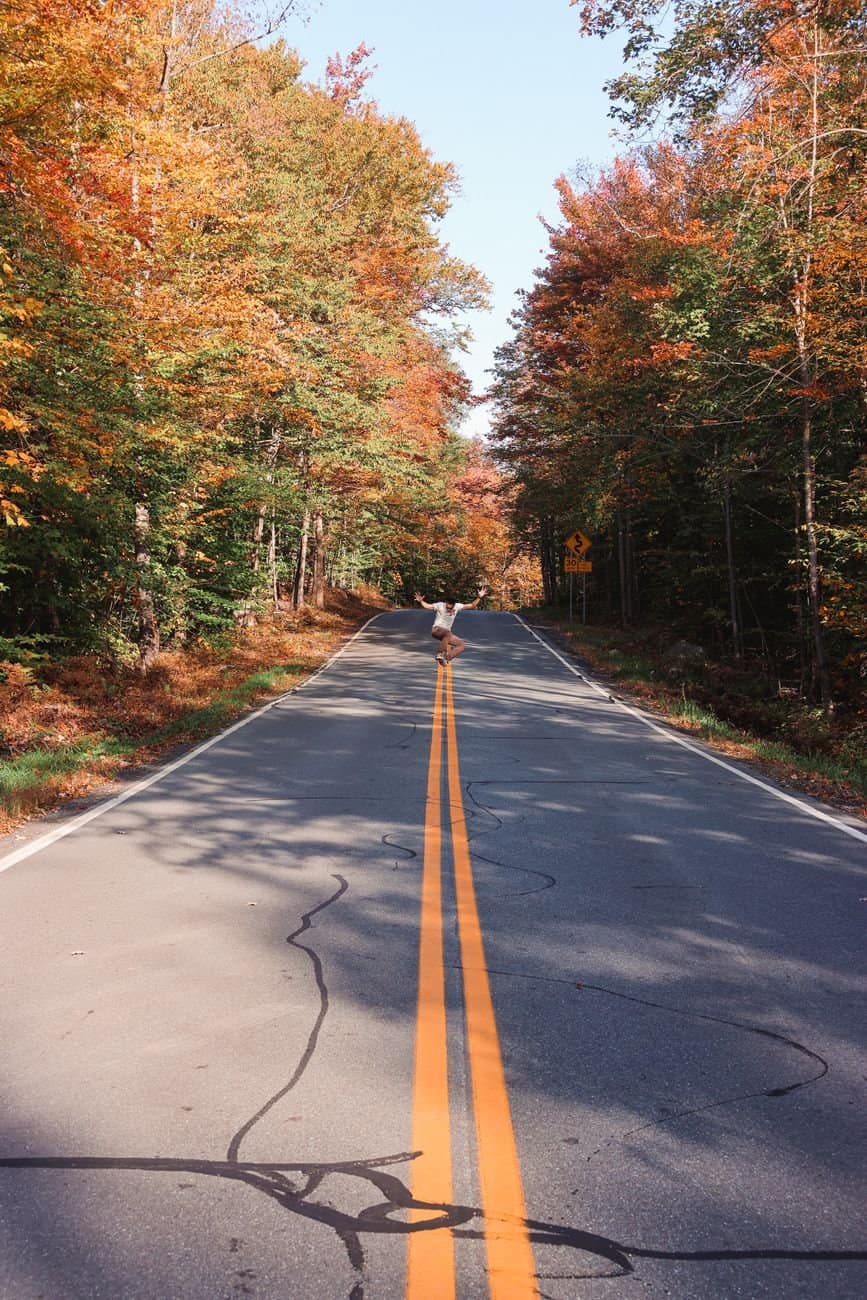 Scenic autumn road in Marshfield, VT with vibrant foliage and clear skies.