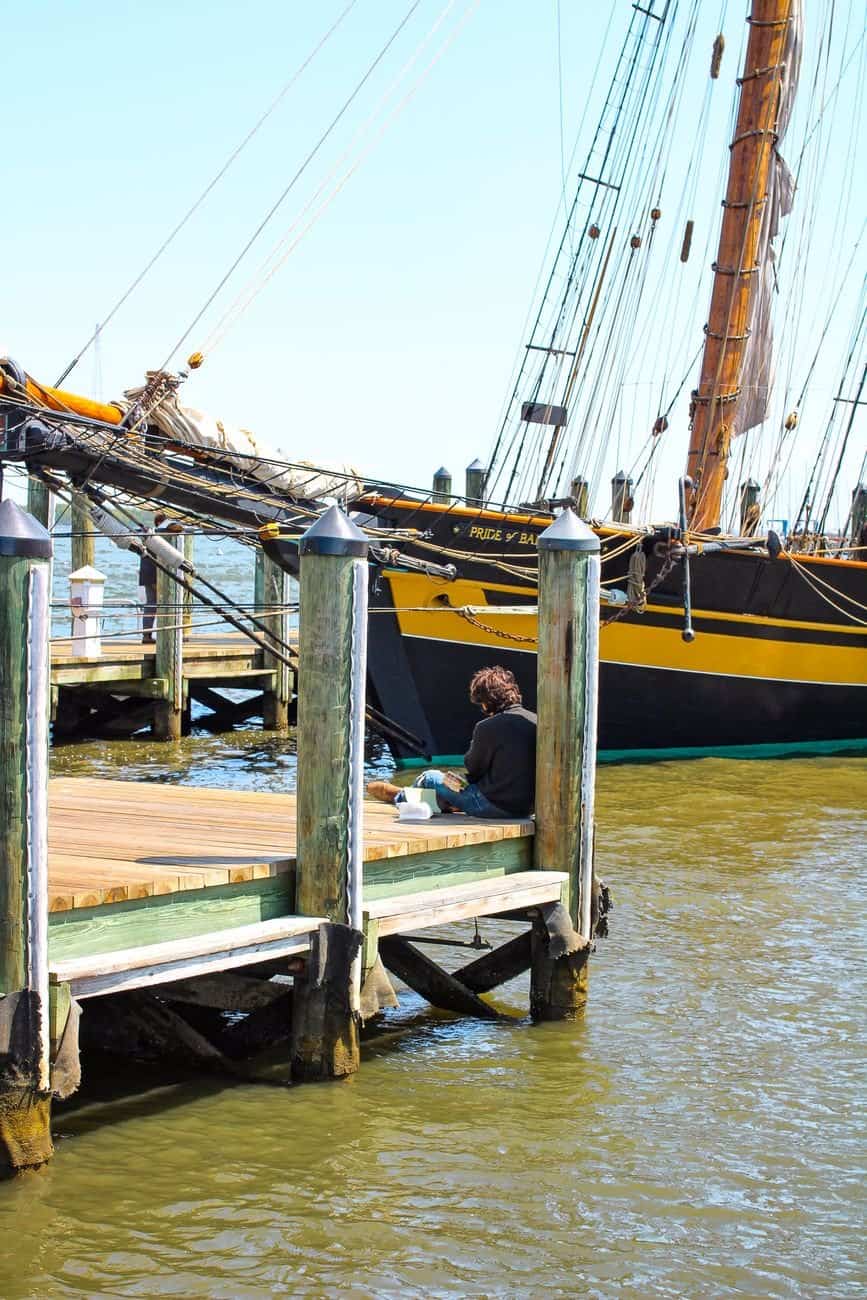 A person sits by a dock with a historic sailboat moored in Annapolis harbor, Maryland.