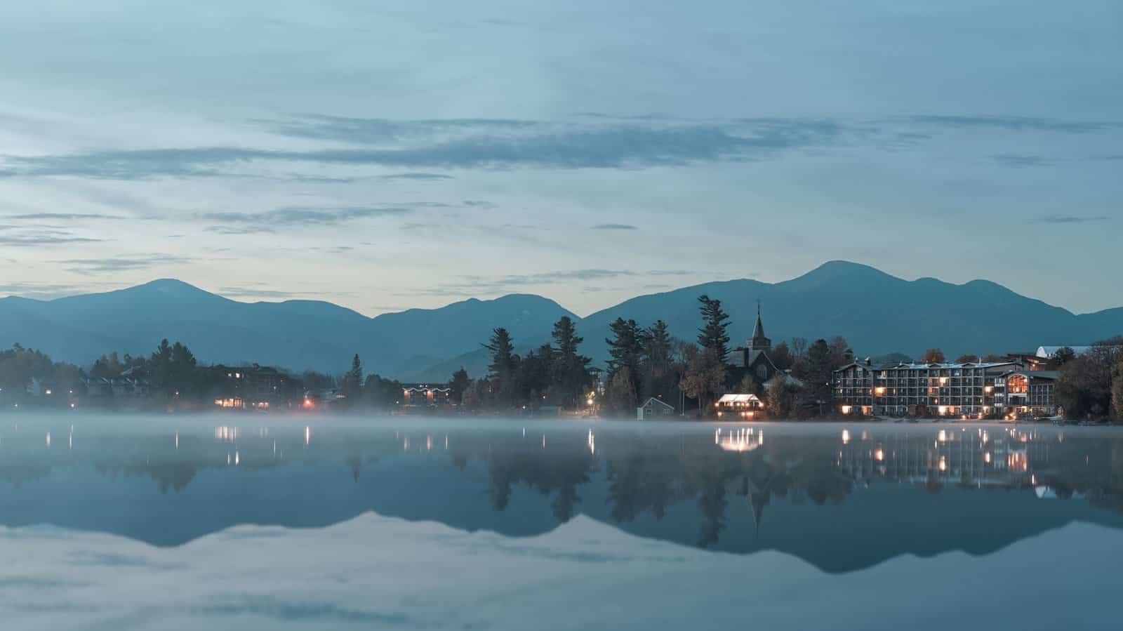 Tranquil morning view of Lake Placid with misty reflections and distant Adirondacks.