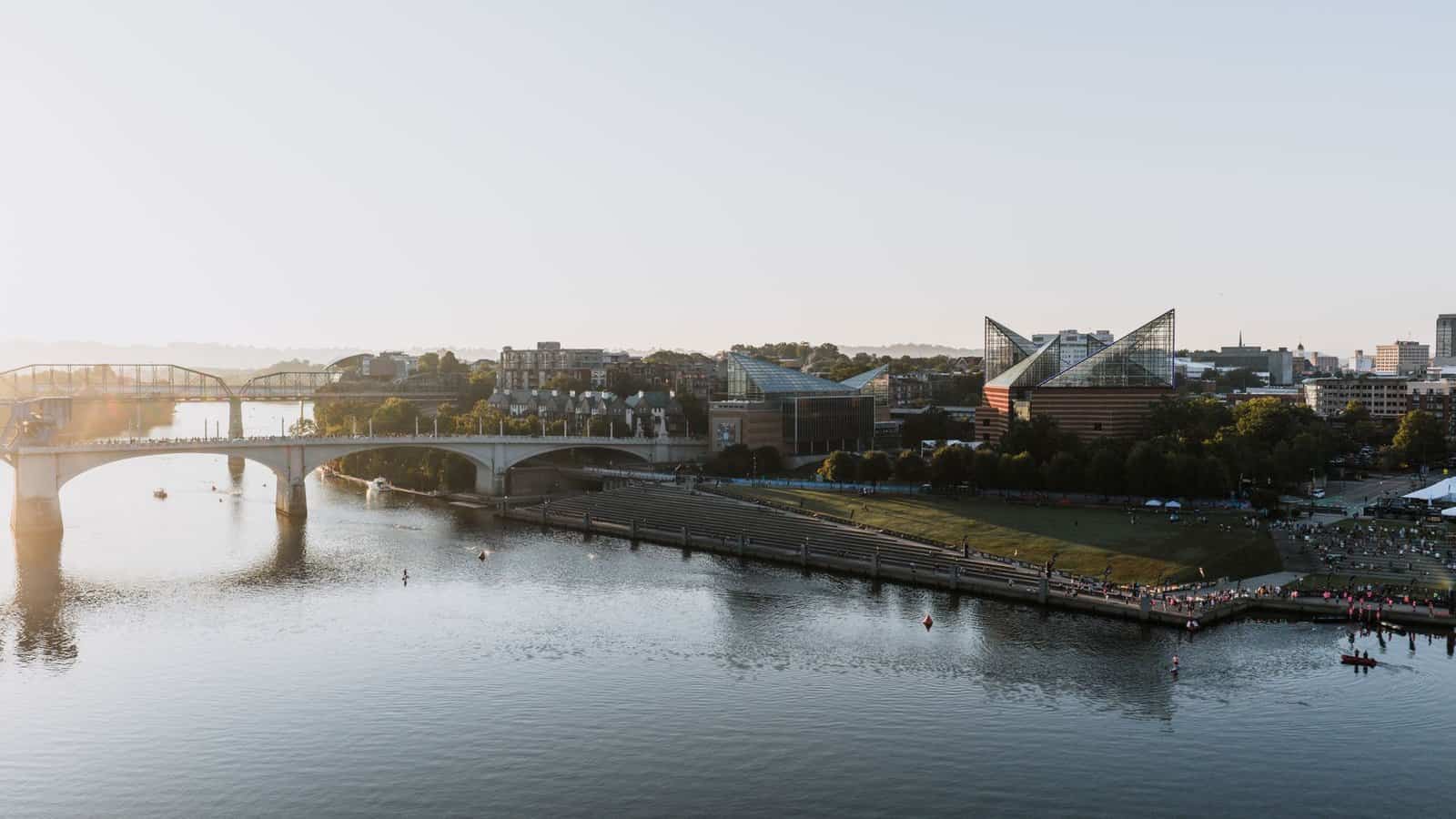 Scenic aerial view of Chattanooga's riverfront and bridges at sunset, showcasing city landmarks and waterfront activities.