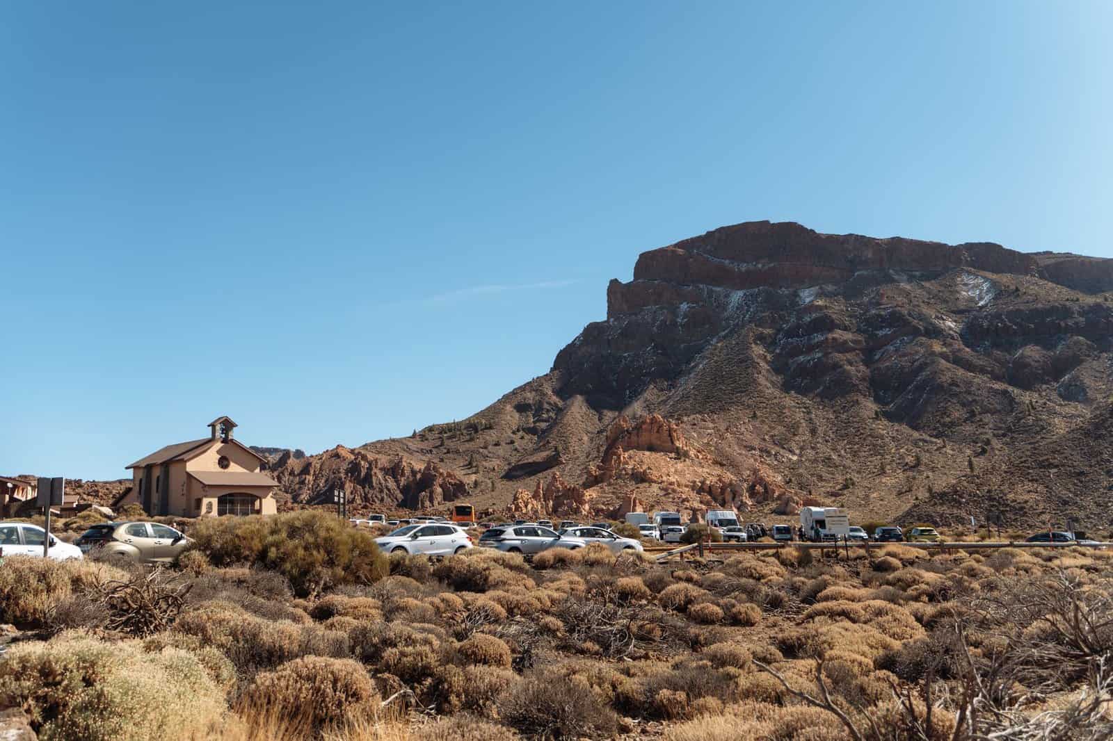 A scenic view of a chapel and cars against rocky mountains in Tenerife.