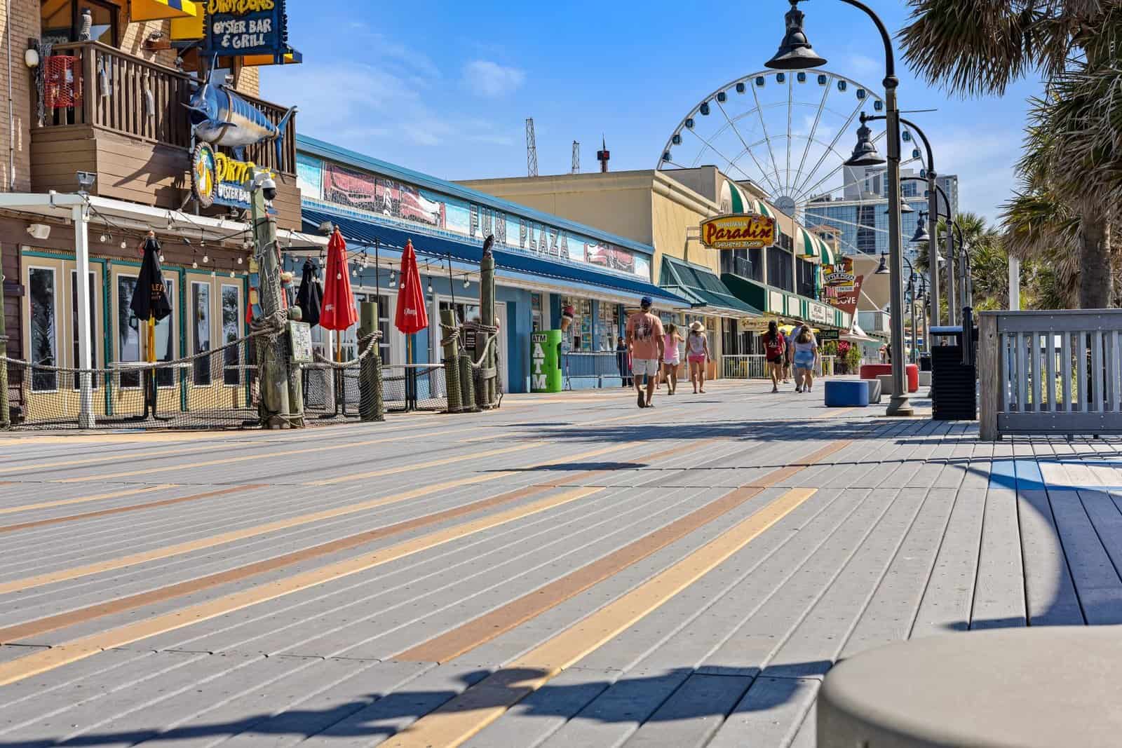 Explore the lively Myrtle Beach boardwalk with shops, a Ferris wheel, and visitors in the summer sunshine.