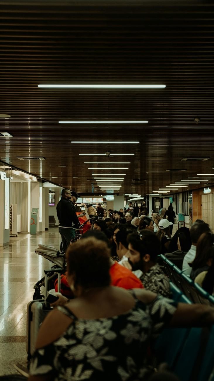Crowded airport waiting area with diverse passengers seated, waiting for flights.